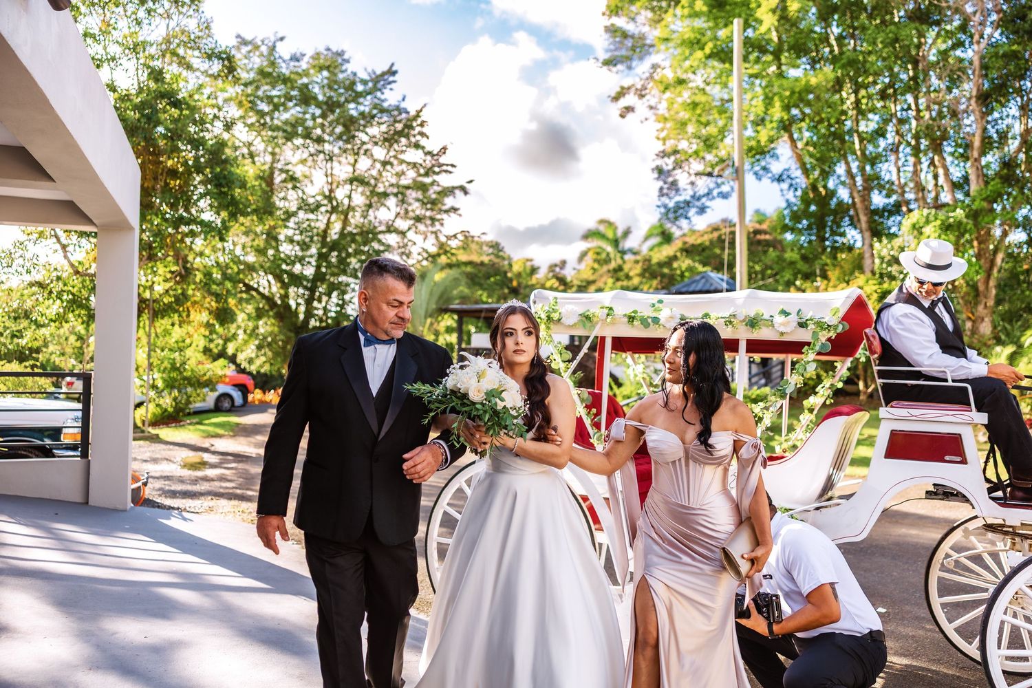 Bride in white gown and groom in black tuxedo exit a horse-drawn carriage at an outdoor wedding venue.