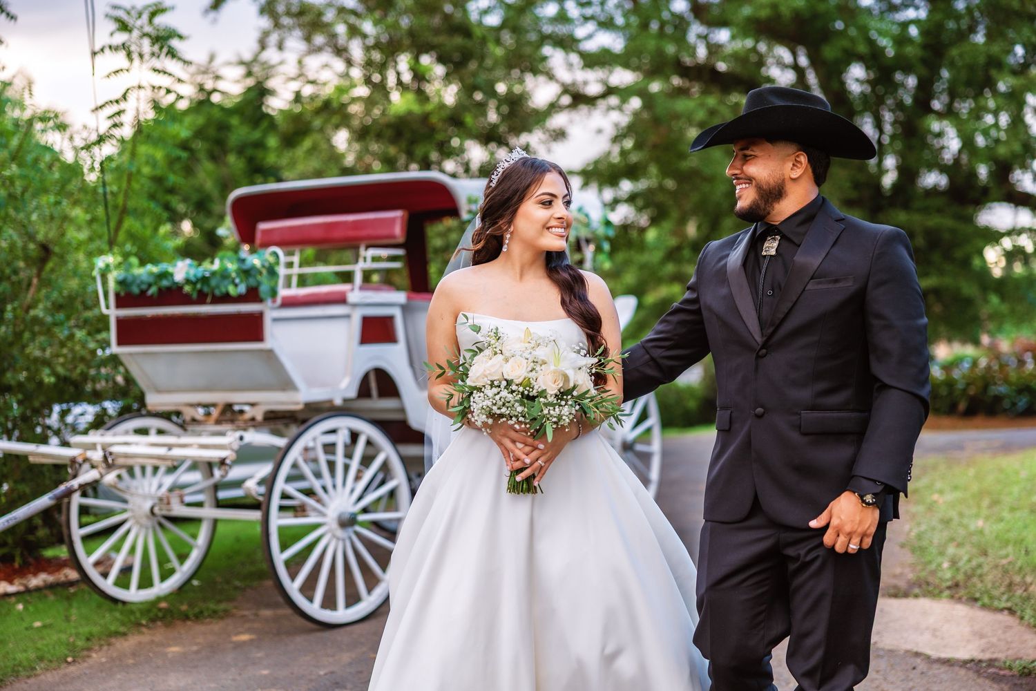 A romantic carriage ride moment with a couple in wedding attire by a white horse-drawn carriage in a garden setting.