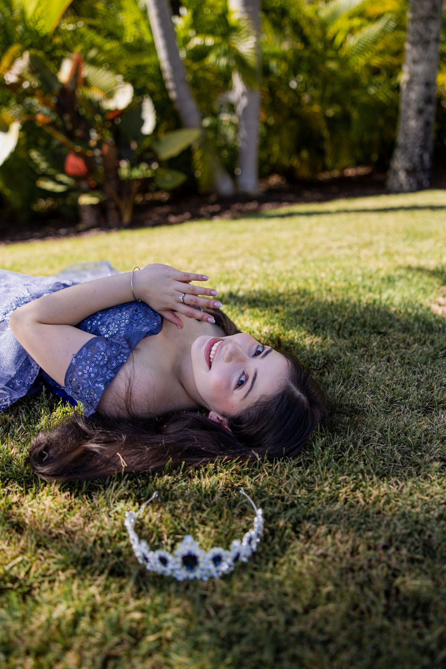 Artistic portrait on grass featuring a blue dress and floral crown in natural lighting.