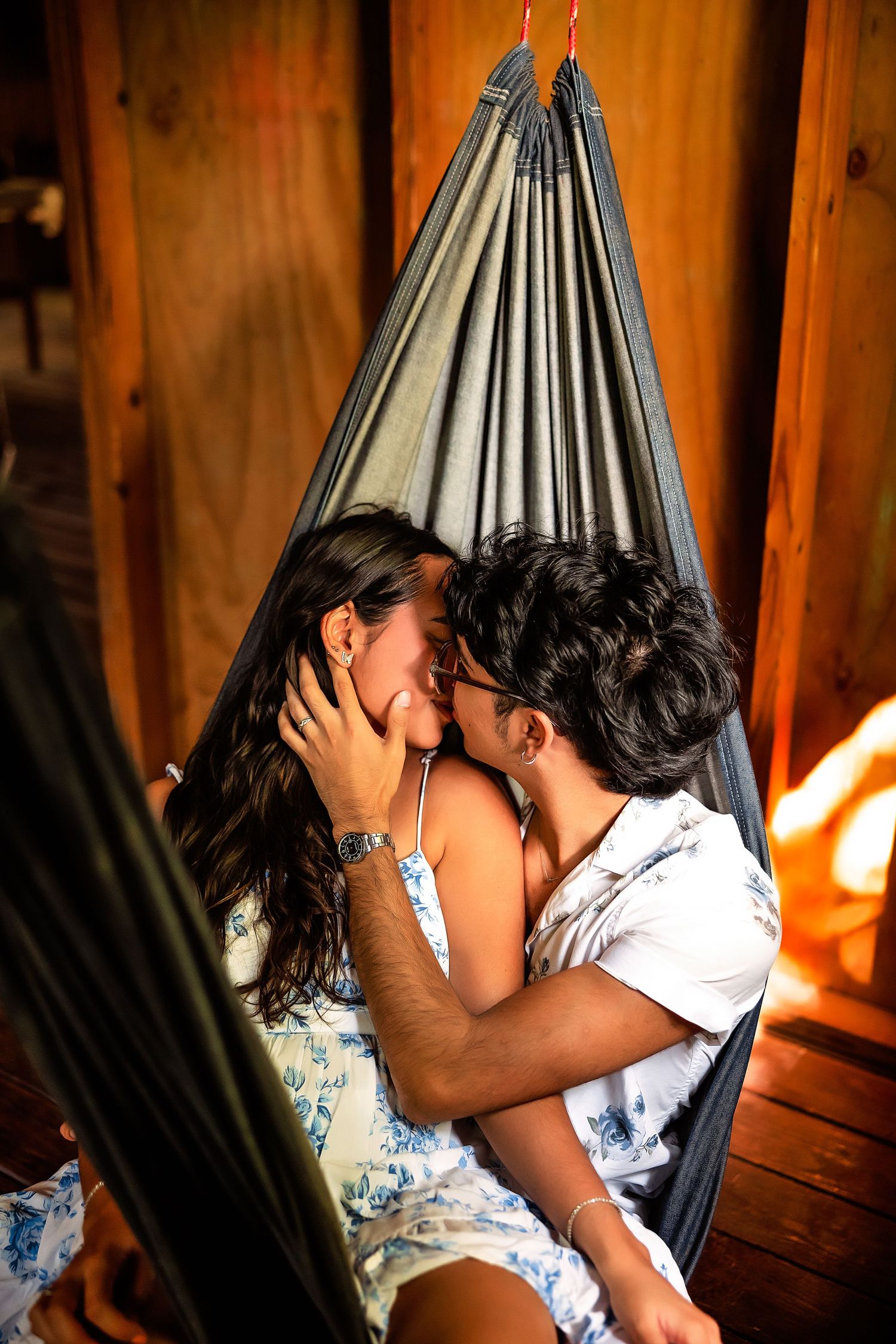 Romantic couple sharing a kiss in a hammock inside a warm wooden cabin with sunlight filtering through.