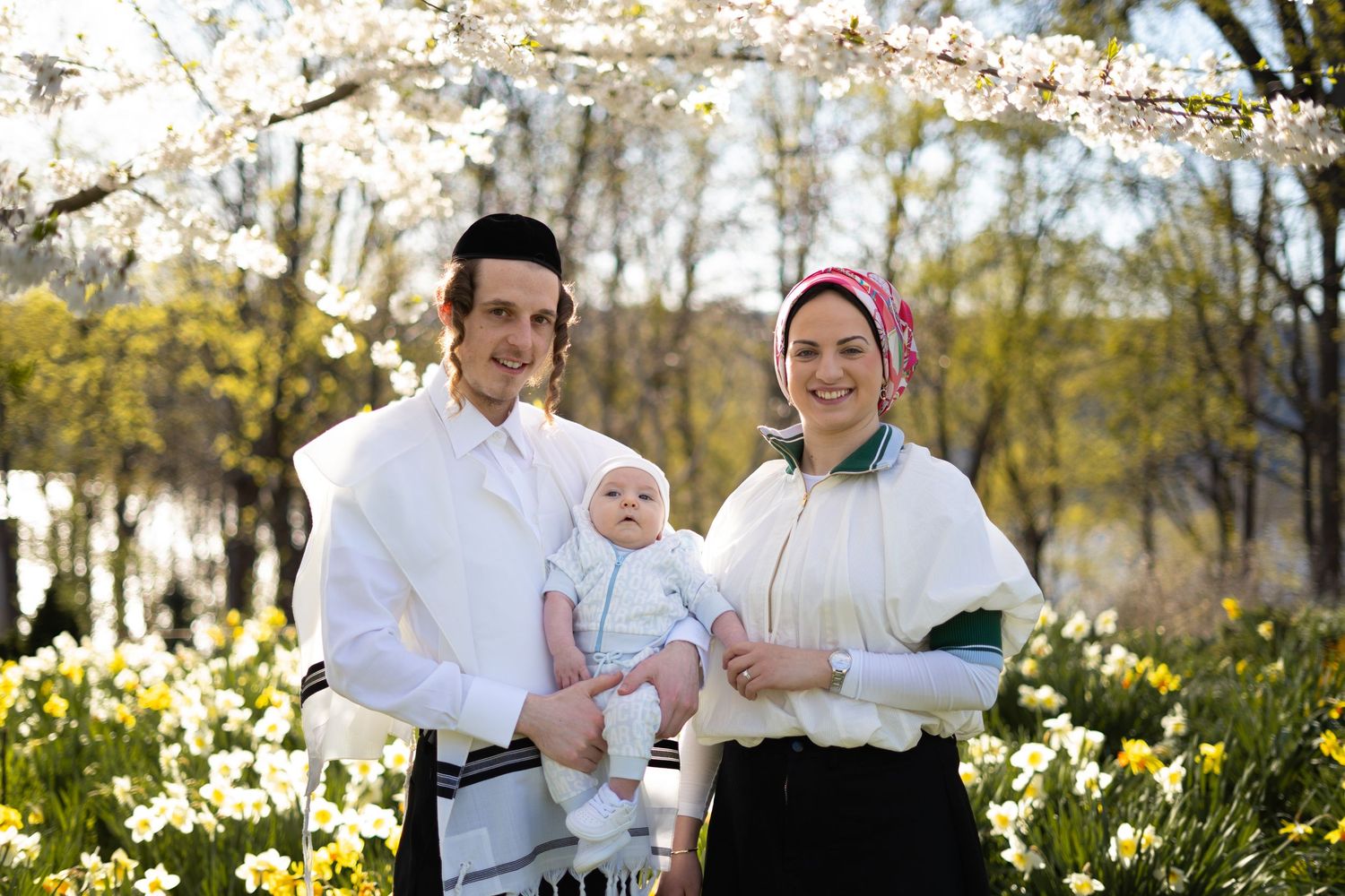 A family in white outfits poses together in a blooming spring garden with cherry blossoms and daffodils in new york
