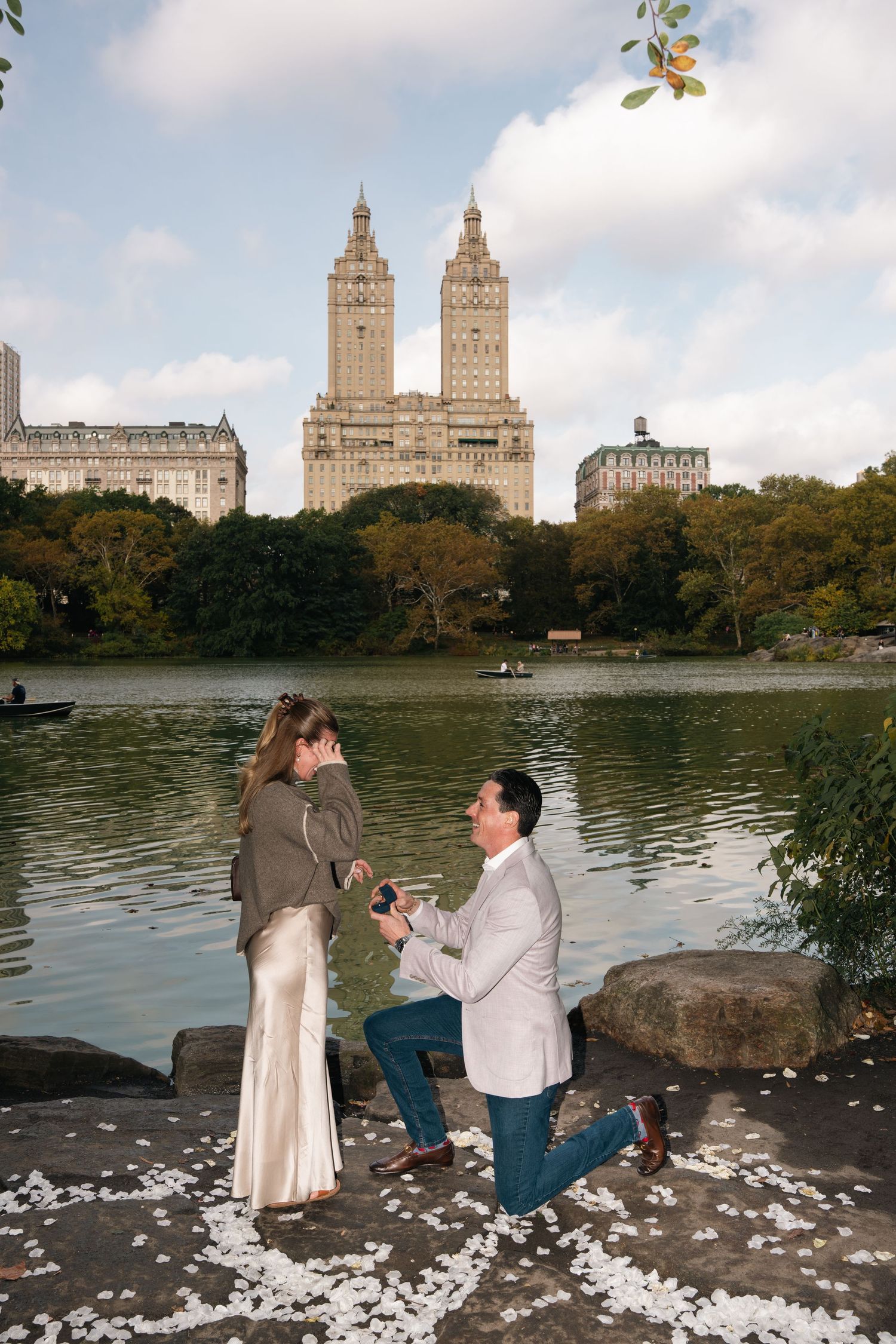 A romantic proposal scene by the lake in Central Park with the iconic San Remo towers rising in the background.