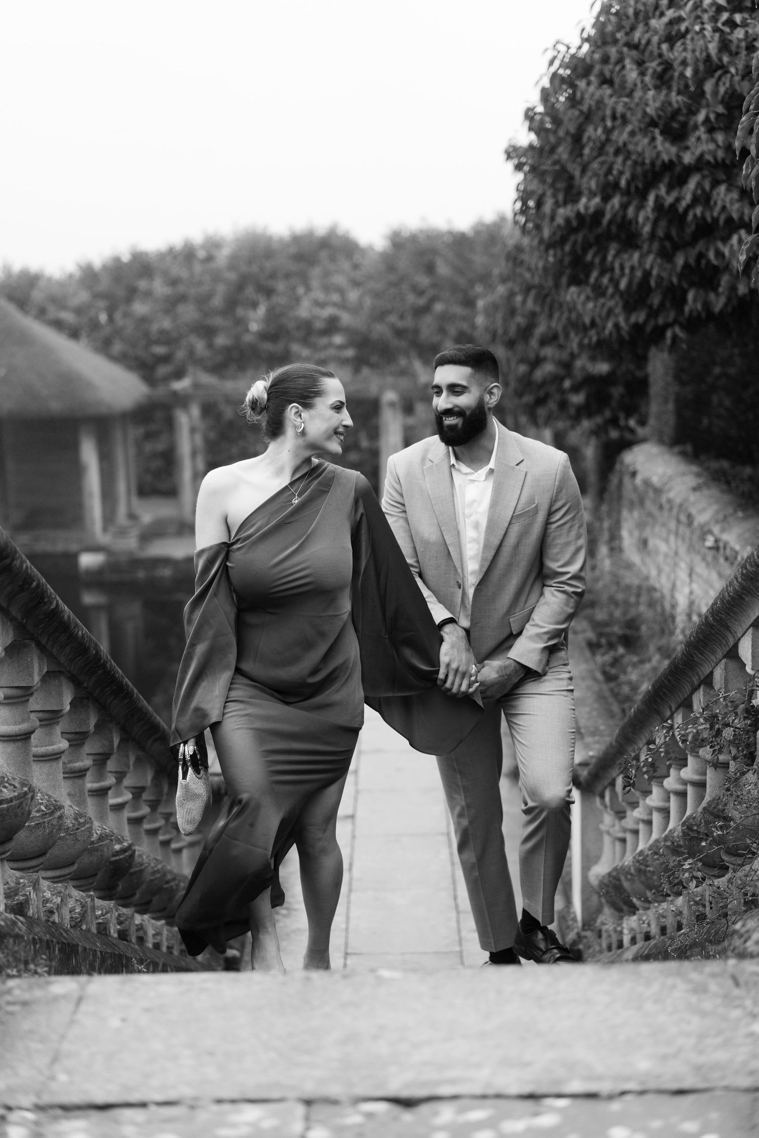 Black and white photo of a couple sharing a moment on stone steps surrounded by greenery.