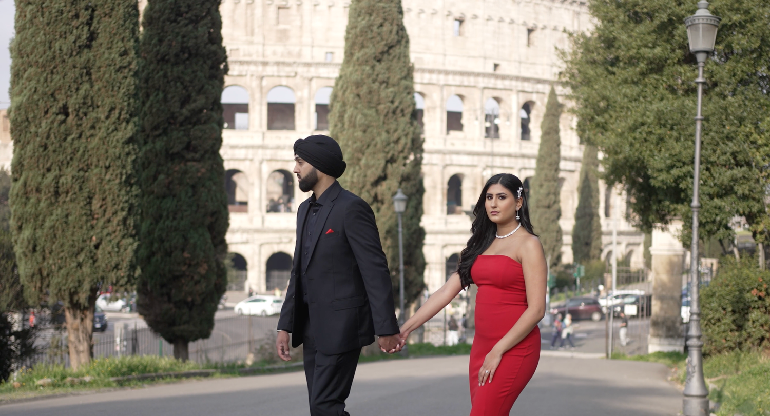 Couple in formal attire walking near the Roman Colosseum, with cypress trees in view.