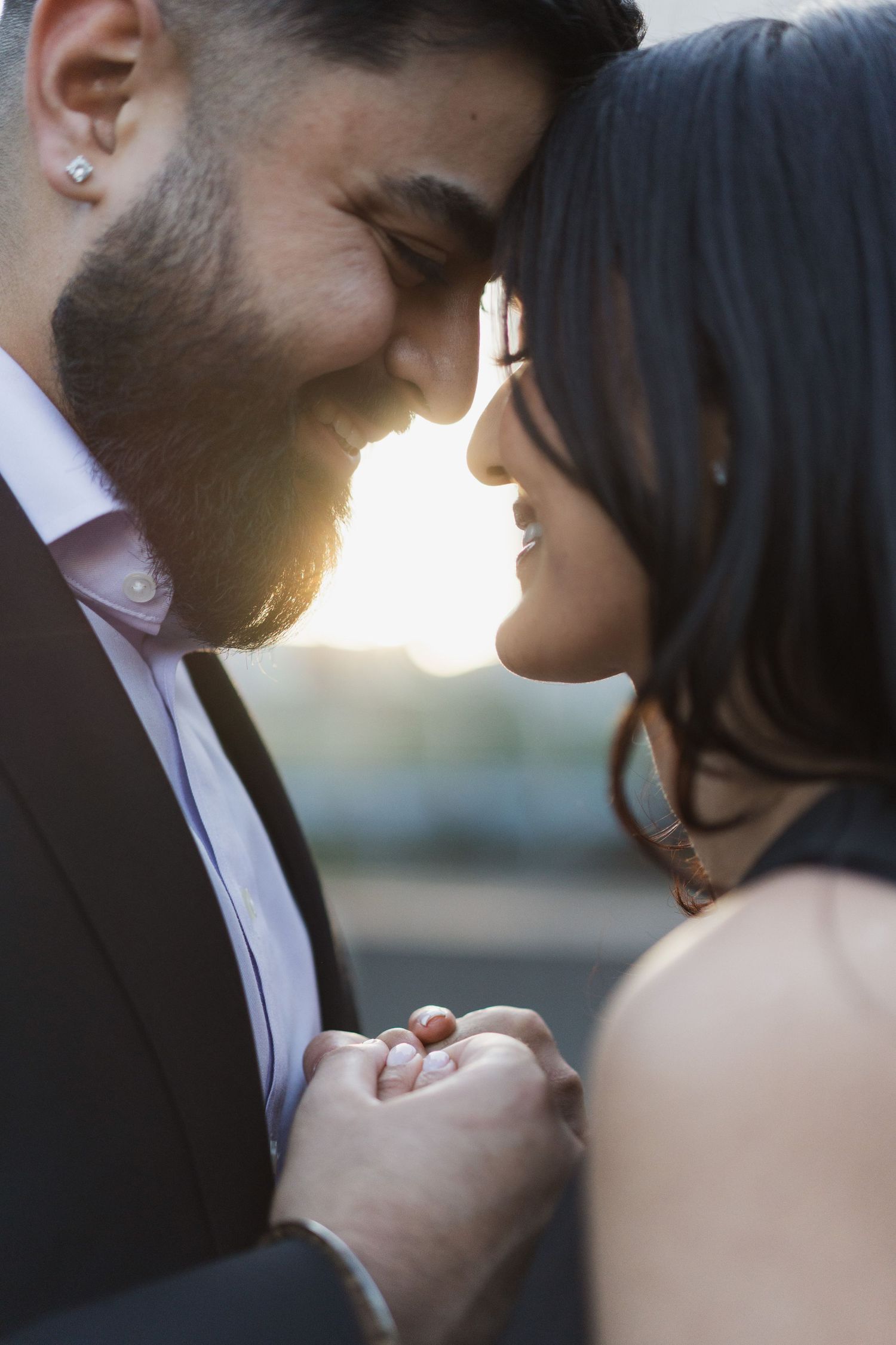 A tender moment between a couple wearing formal attire as they hold hands and smile with sunlight in the background.