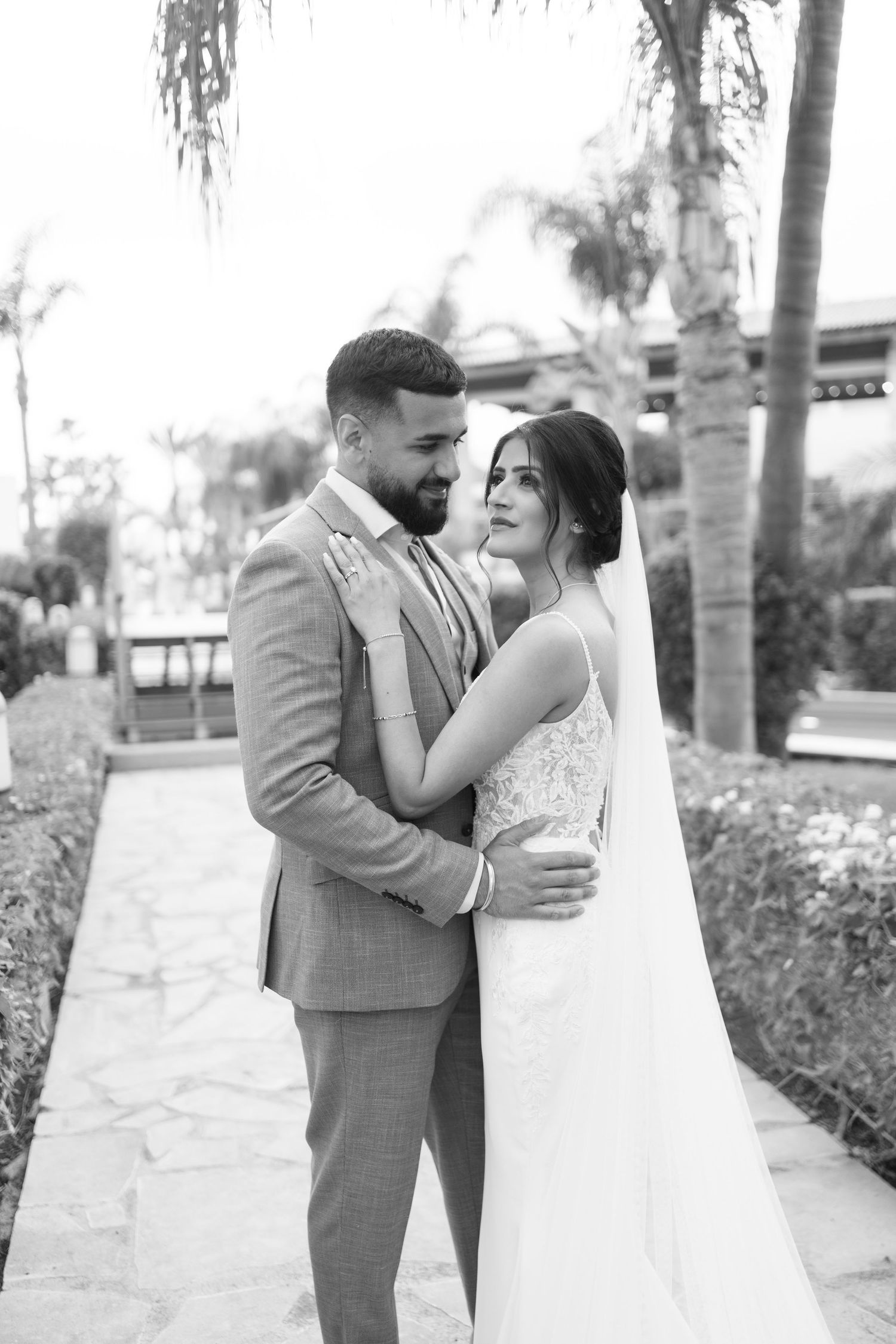 Black and white portrait of a couple in wedding attire among palm trees.
