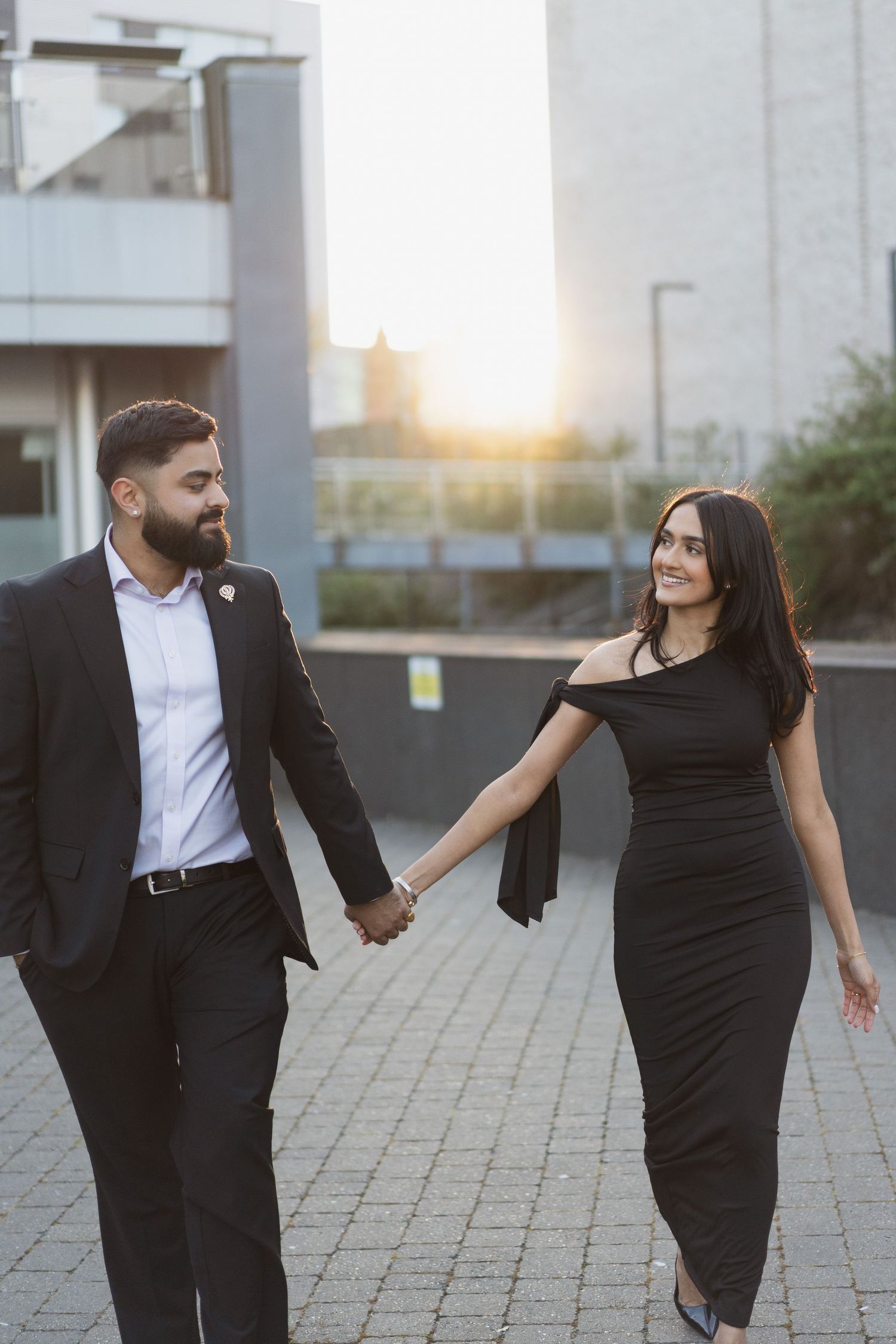 Stylish couple walking hand in hand on urban street at sunset.