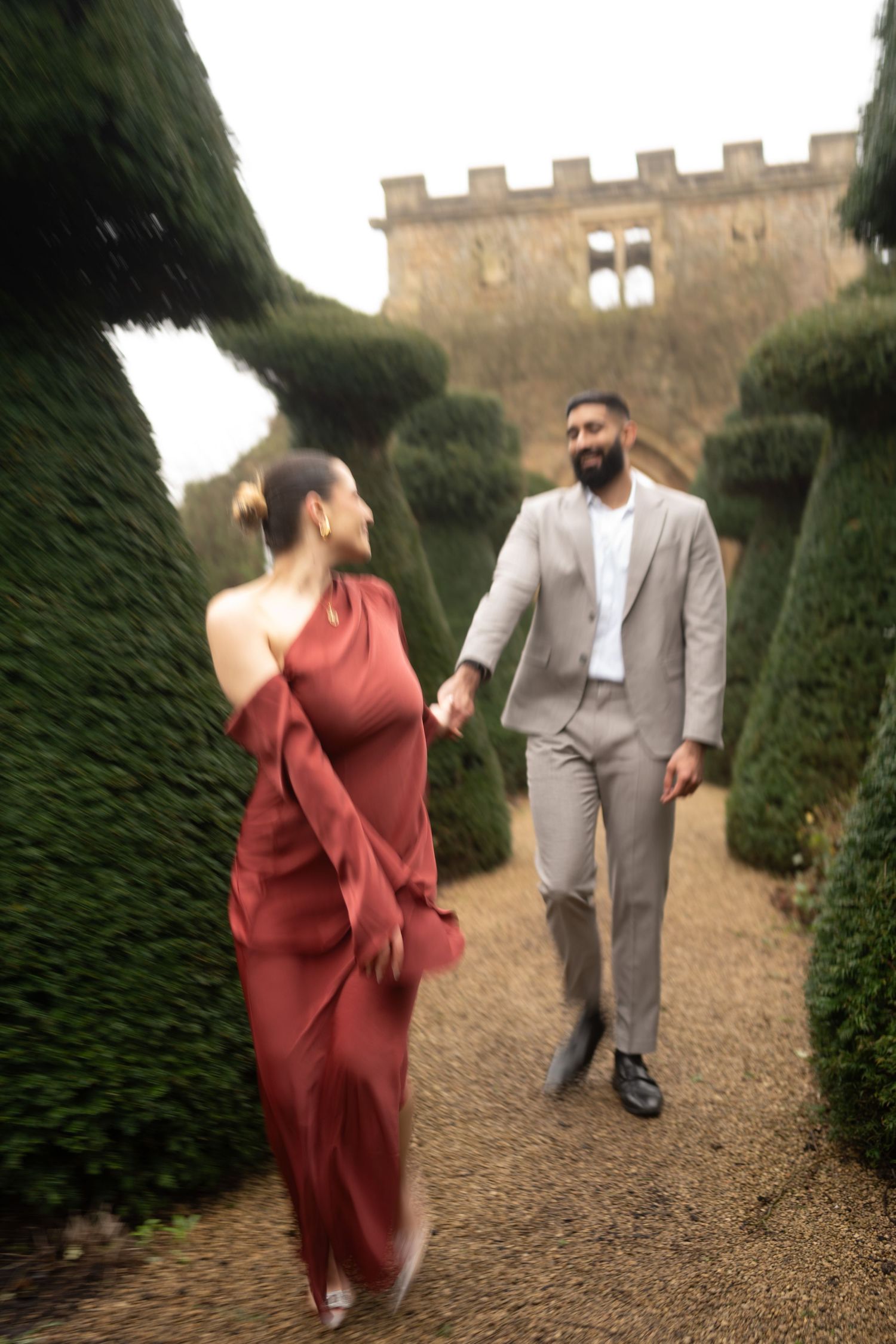 Couple walking through manicured garden path with castle walls and topiary.