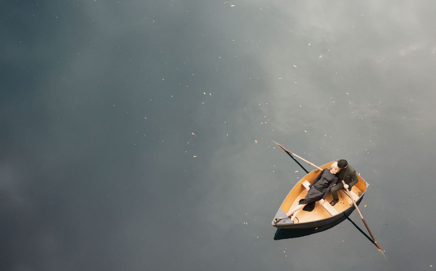 Aerial view of a small rowboat floating on dark reflective water against a moody cloudy sky.