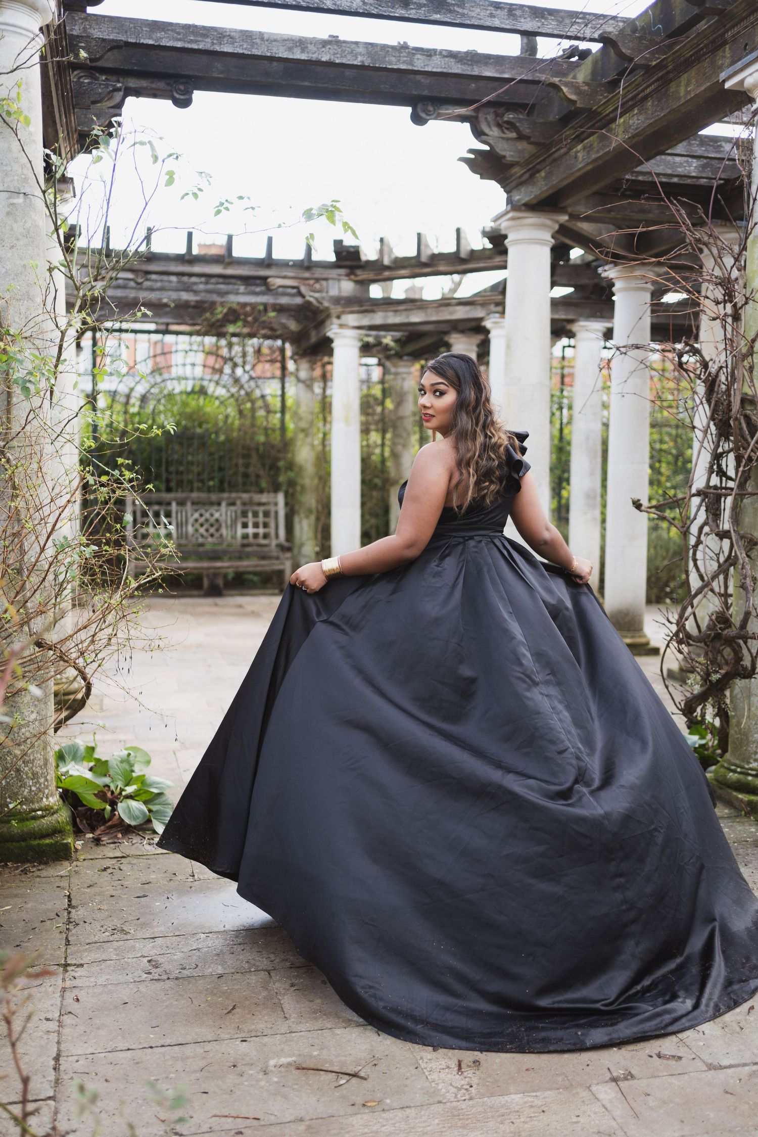 Dramatic photo of a black ballgown in a garden pergola setting.