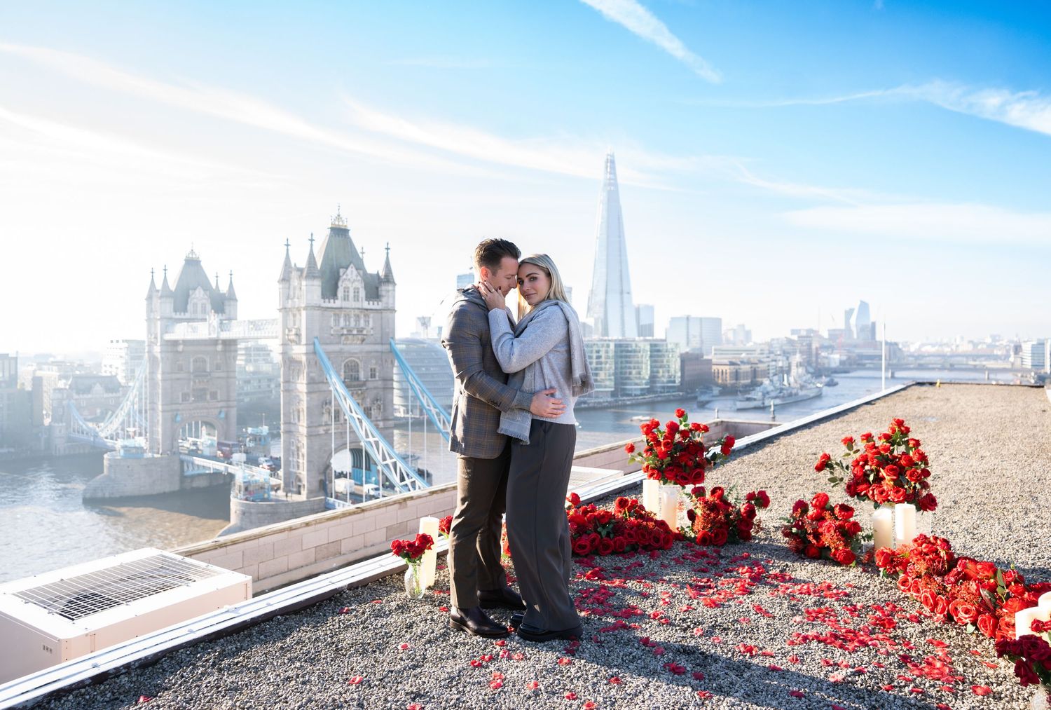 A romantic engagement session at London Bridge with a sea of red rose petals scattered around the couple against the city skyline.