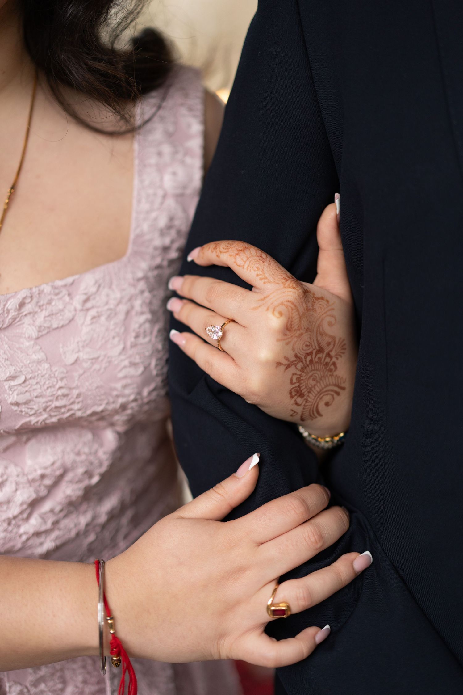 Close-up of hands showing henna designs and engagement ring against formal attire.