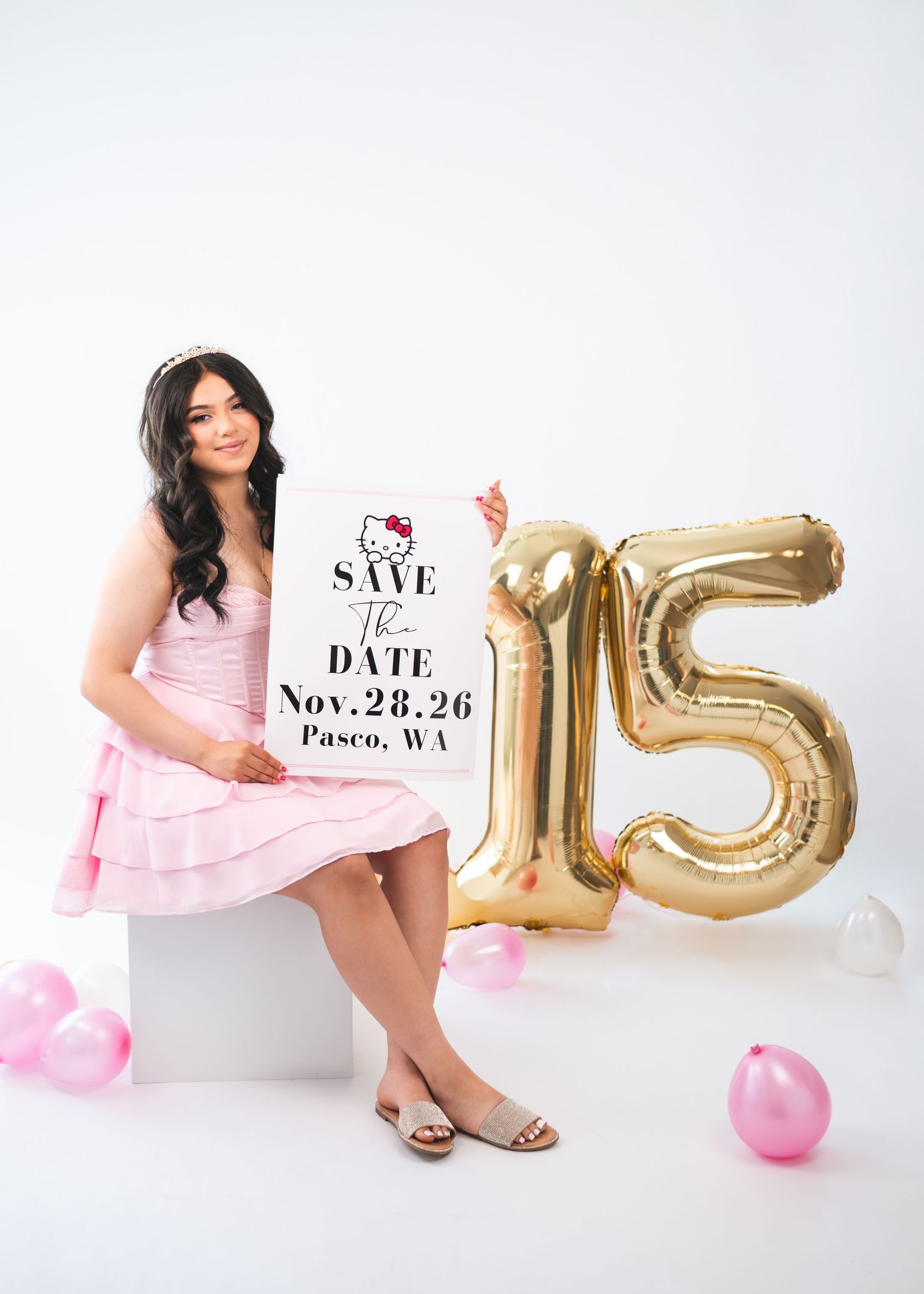 Young woman in pink dress holds Save the Date sign beside gold number 15 balloons for a quinceañera in Pasco, WA.