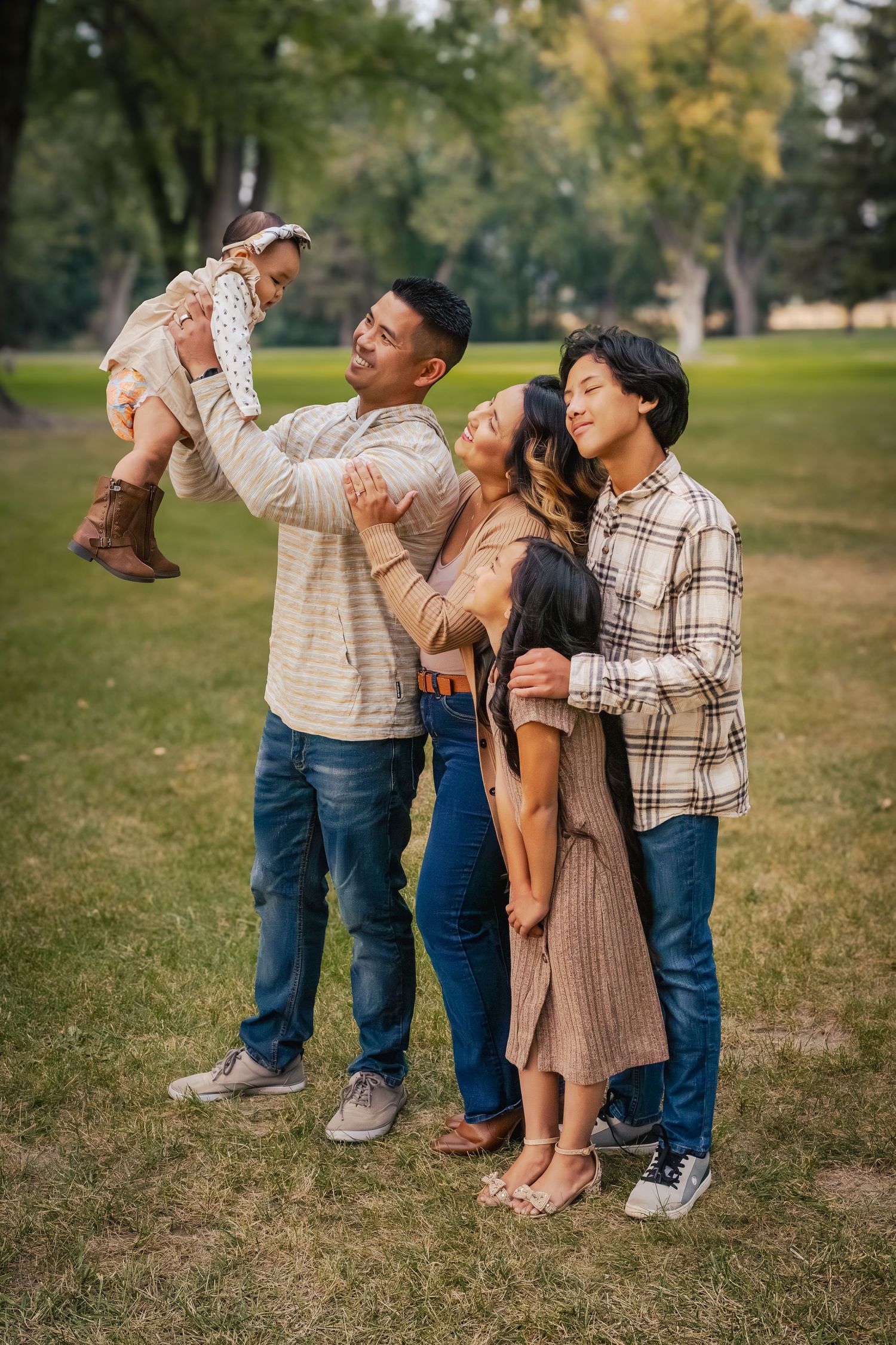 A family enjoys a playful moment together on grass in a park during autumn.