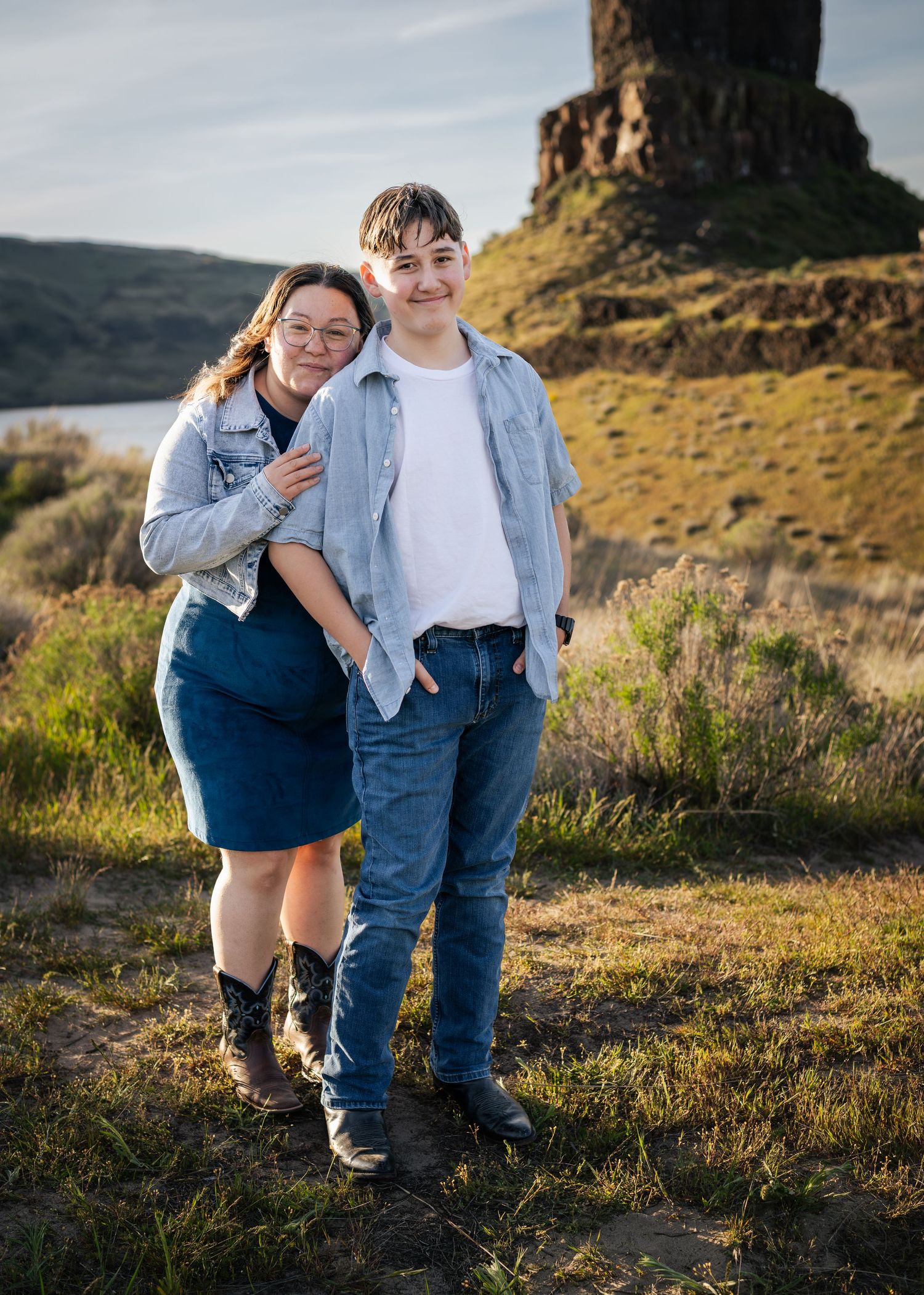 Couple posing outdoors near a rocky butte, wearing denim outfits, smiling in a scenic landscape.