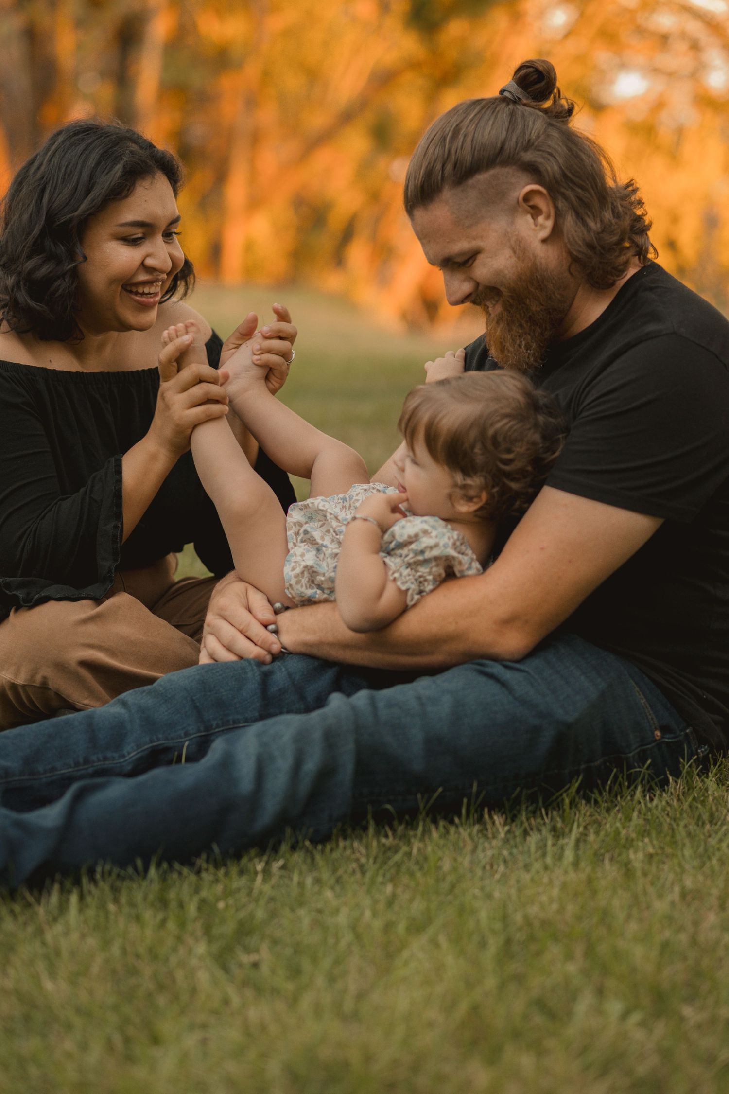 A family lies together on grass during golden hour, sharing playful and tender moments in a sequence of candid shots.