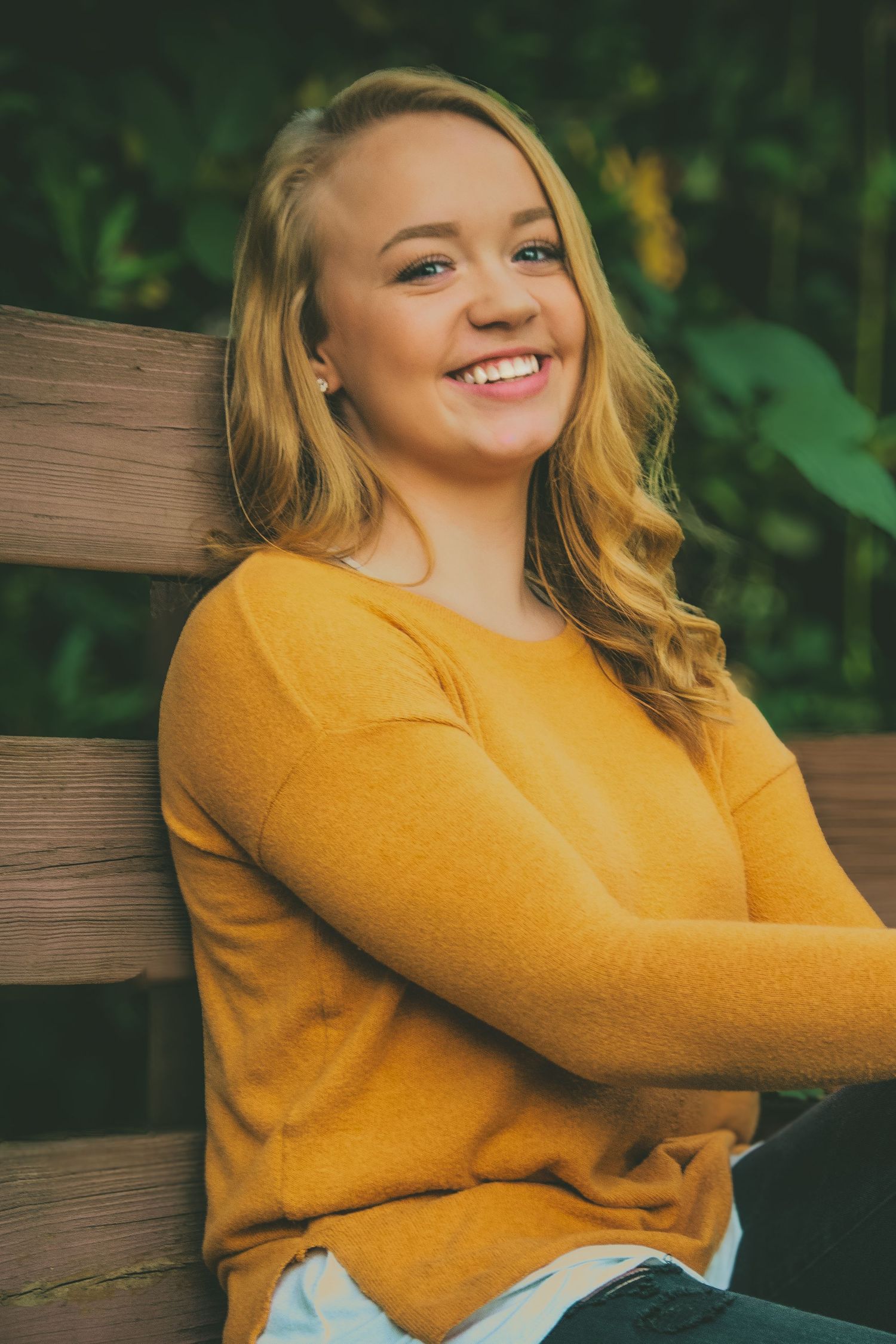 Woman in yellow sweater poses for casual outdoor portraits against green foliage.