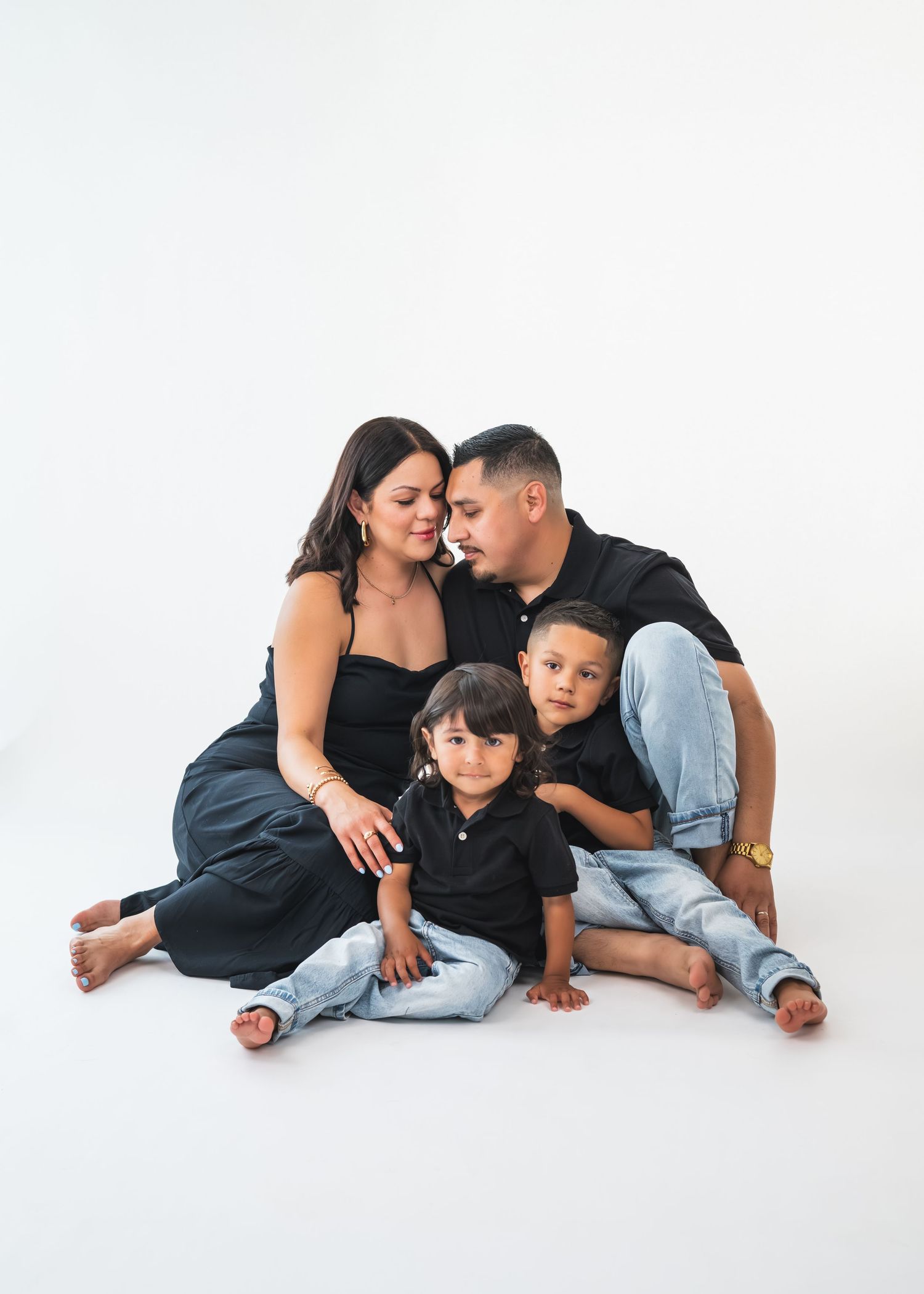 A family of four in matching black tops and jeans poses together on a white studio background.