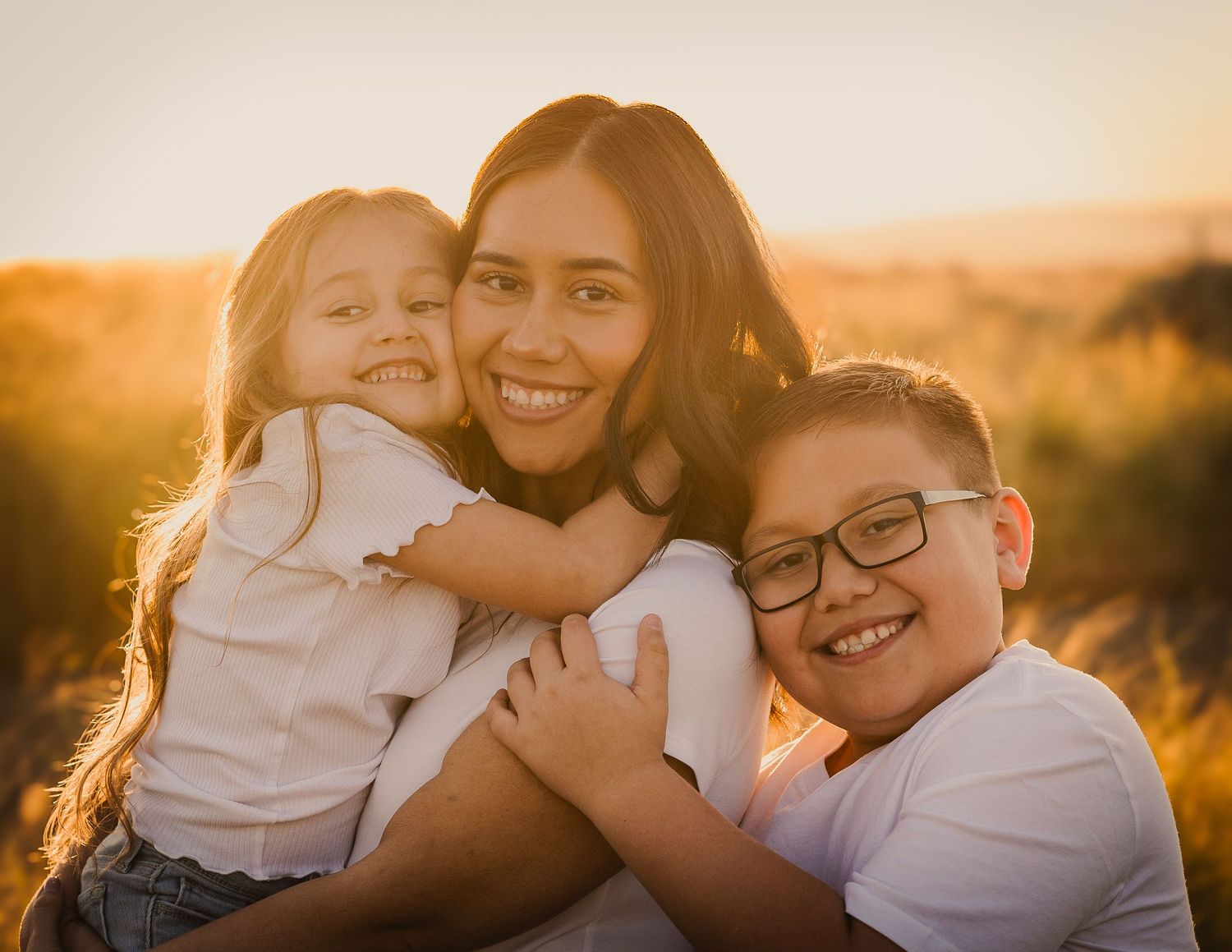 Family embracing and smiling together during golden hour sunset photoshoot outdoors.