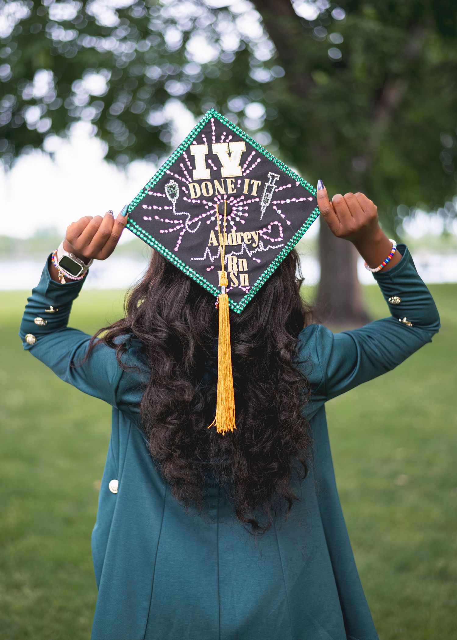 Graduate holds decorated cap reading I've Done It with name Audrey Min BSN, wearing teal blazer outdoors.