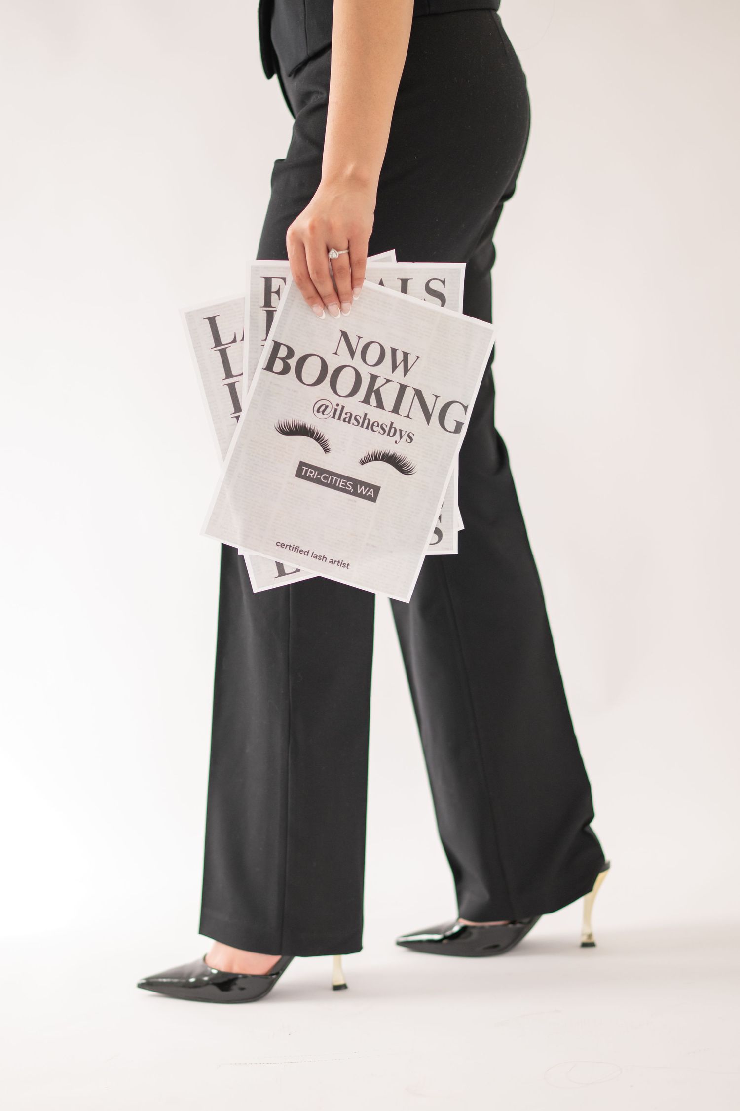 Professional business attire shown from waist down with black wide-leg pants and printed papers in hand against white backdrop.