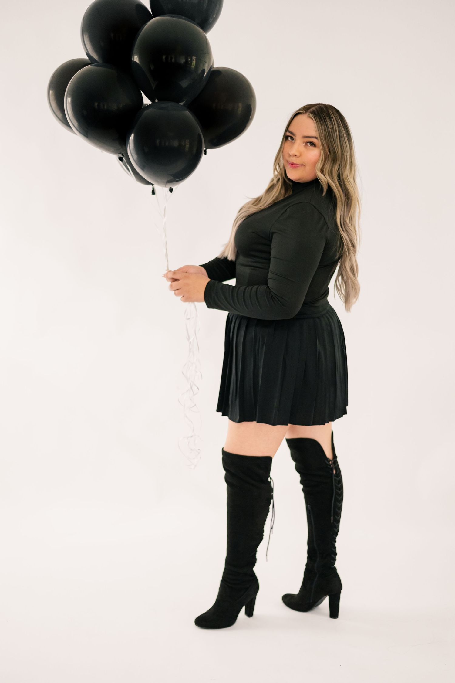Woman in black dress and boots holding black balloons against white backdrop. Washington State birthday photoshoot.