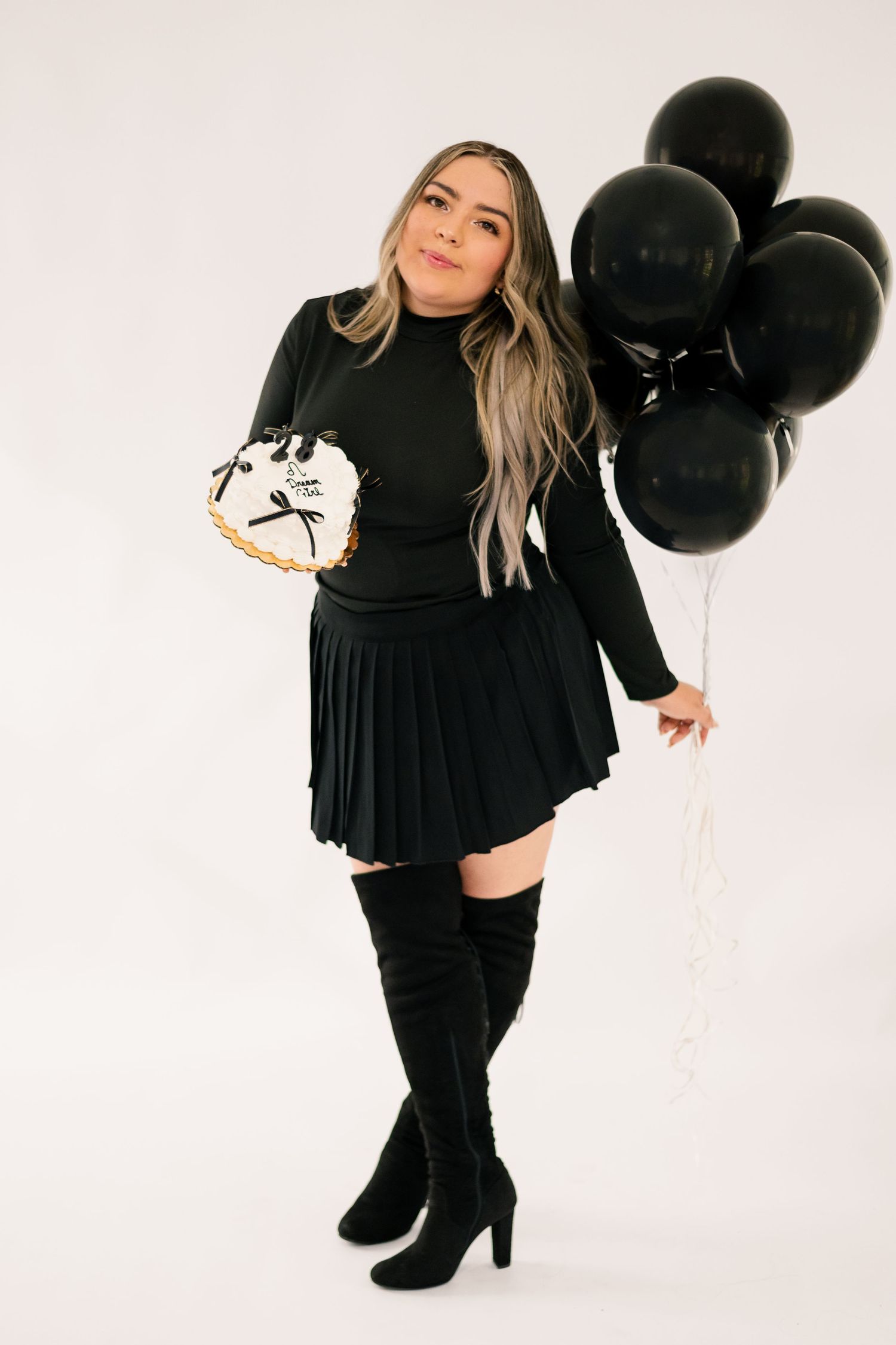 A woman in a black dress poses with black balloons against a white backdrop in a series of studio photos.