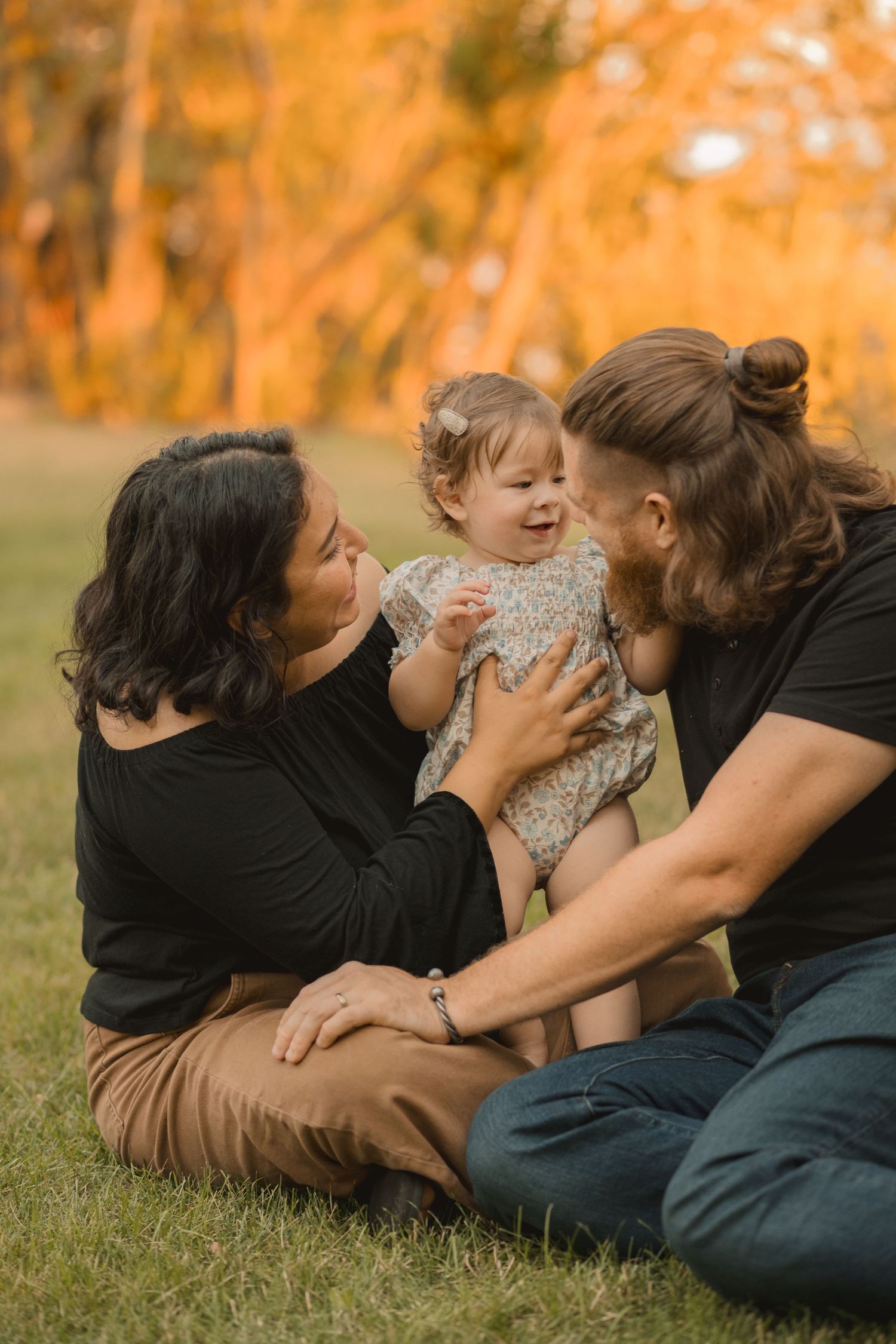 A family lies together on autumn grass sharing tender moments and laughter in a series of candid outdoor photos.
