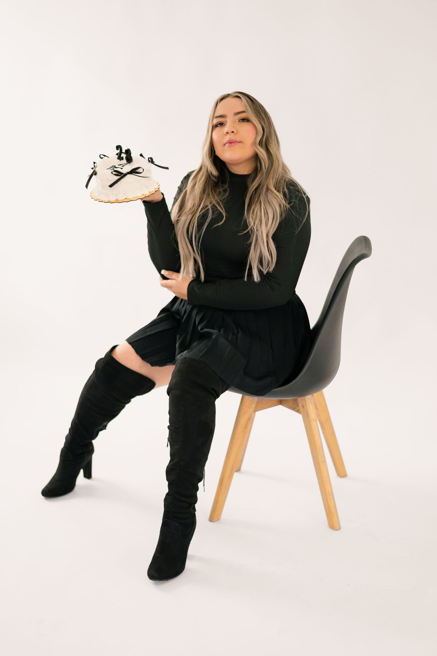 Person in all black outfit poses on modern chair against white background in artistic fashion photoshoot series.