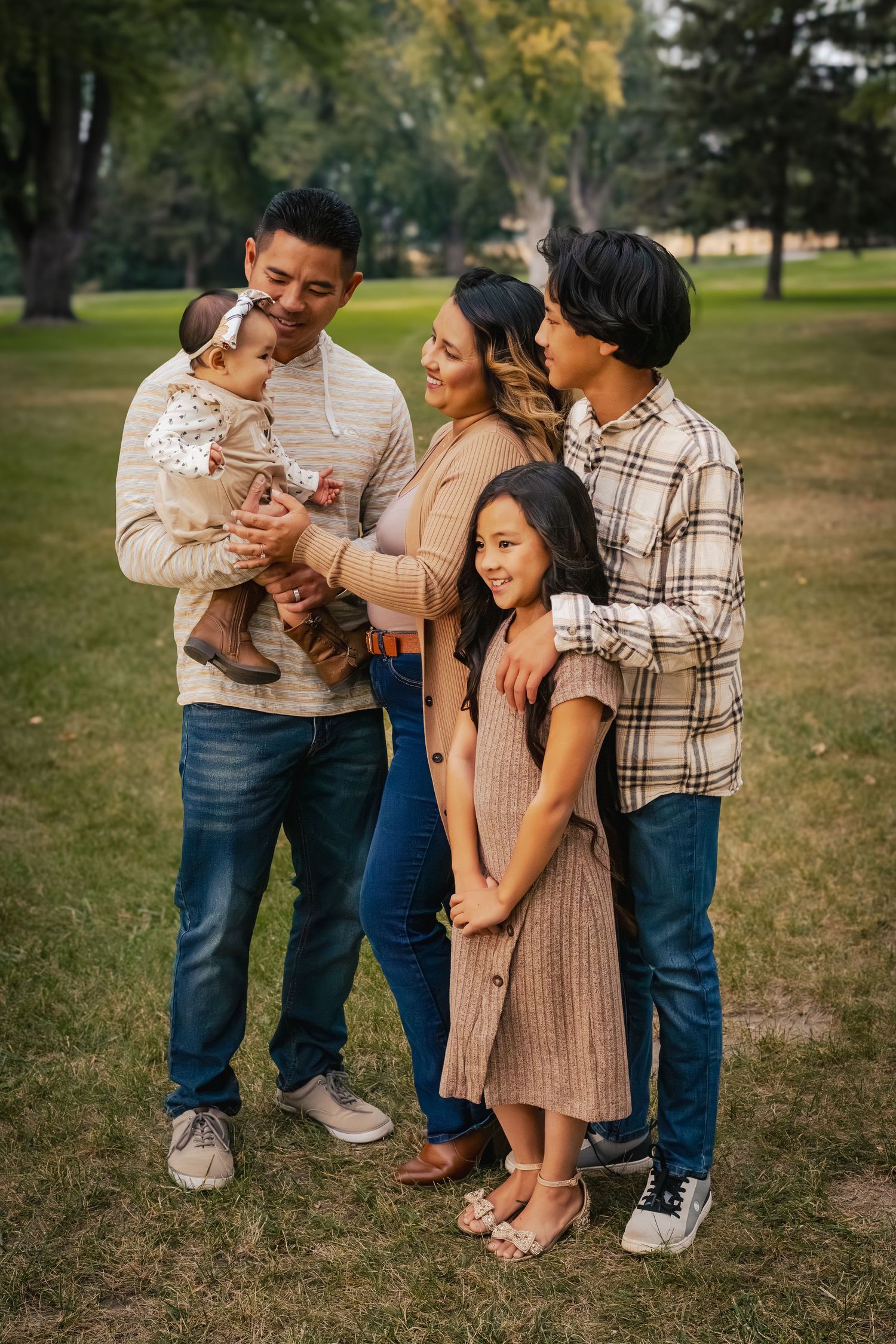 Family in coordinating neutral outfits shares candid moments together during outdoor photo session in a park.
