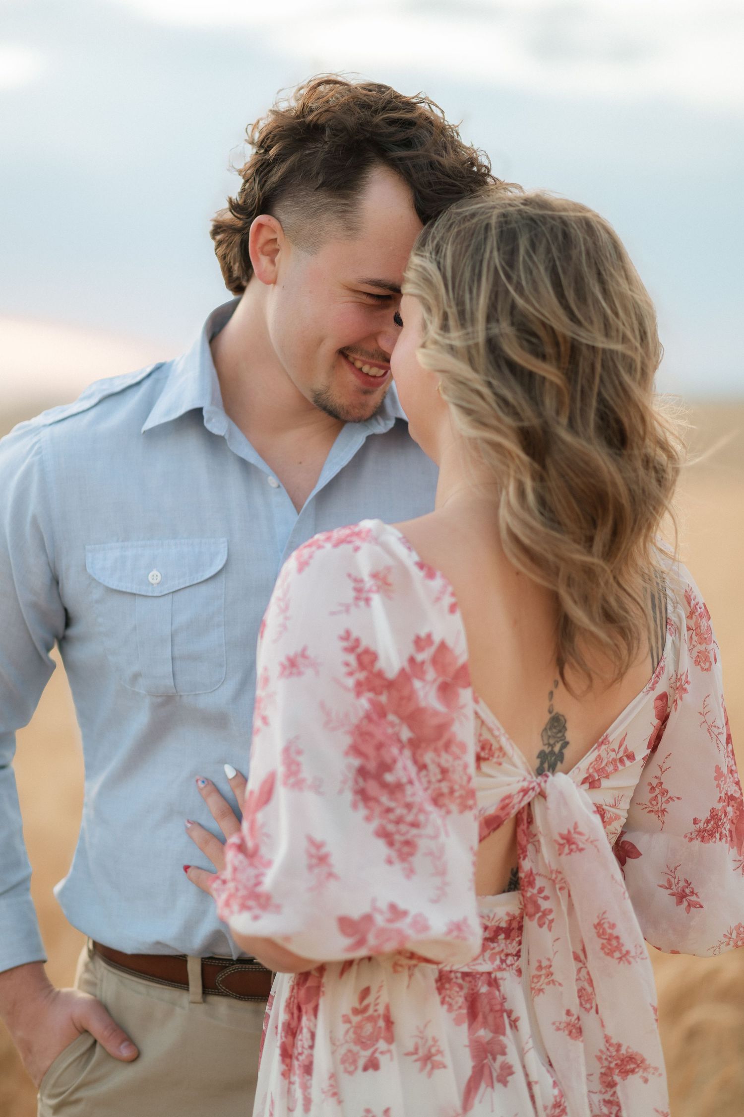 A romantic couple in casual attire share intimate moments in a wheat field at sunset.