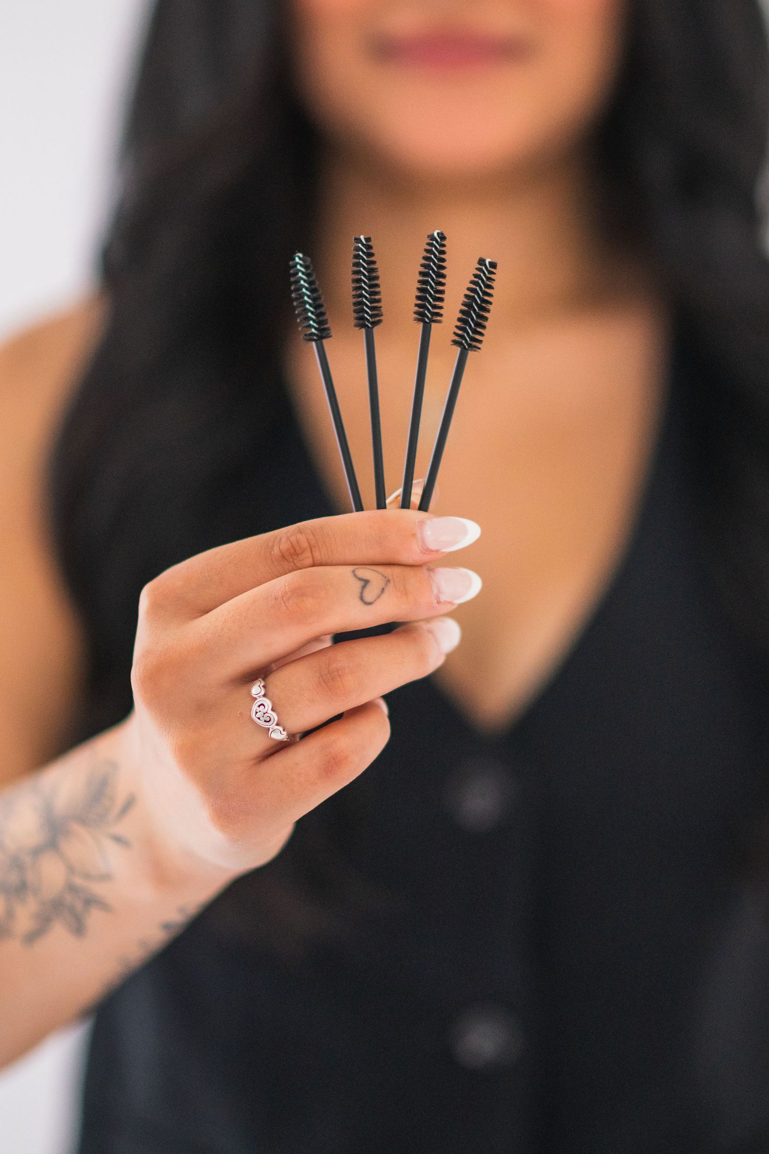 Close-up of hands holding small black mascara wands against white background.