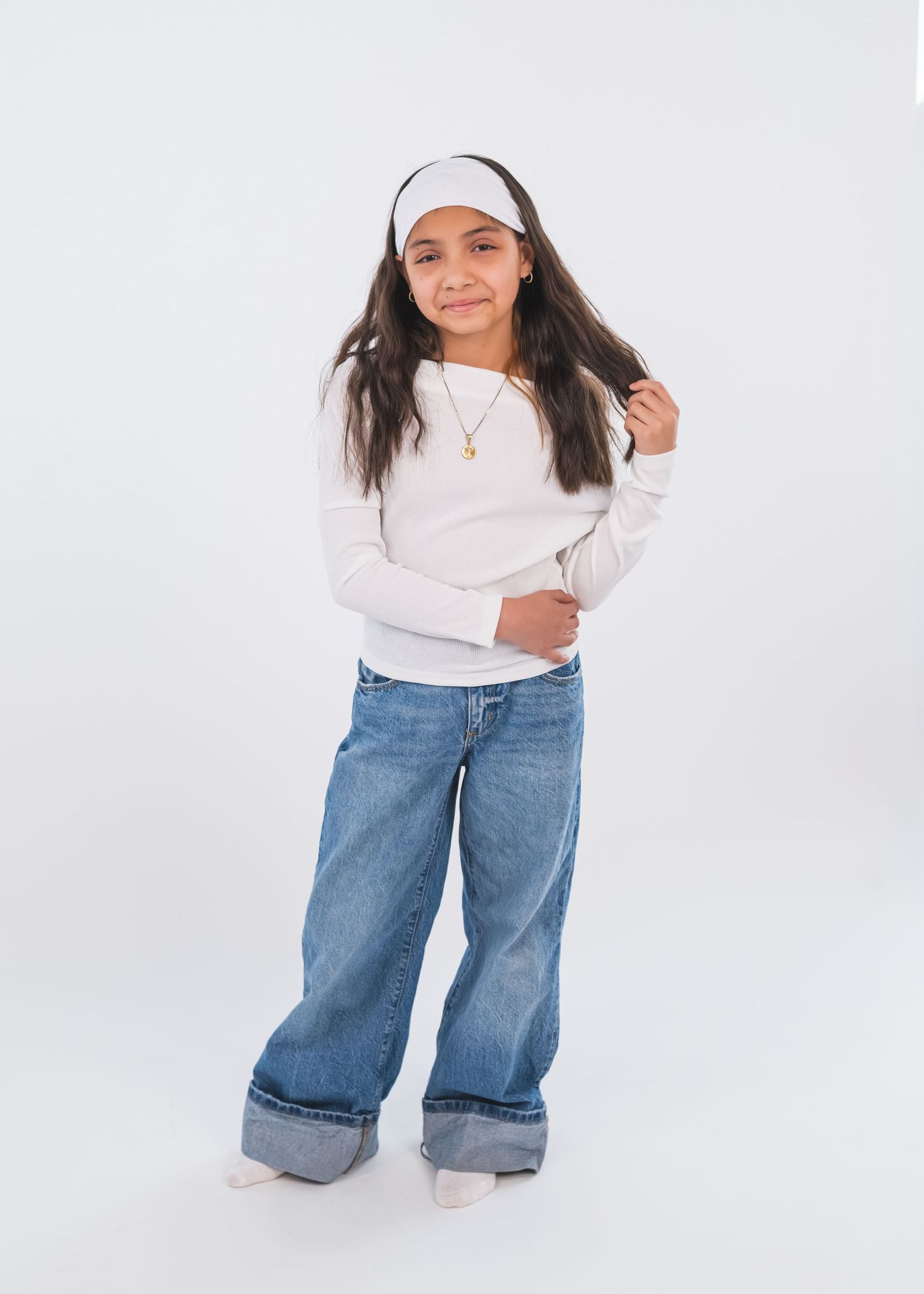 Girl in wide-leg jeans, white long-sleeve top, and headband poses confidently against a white background.