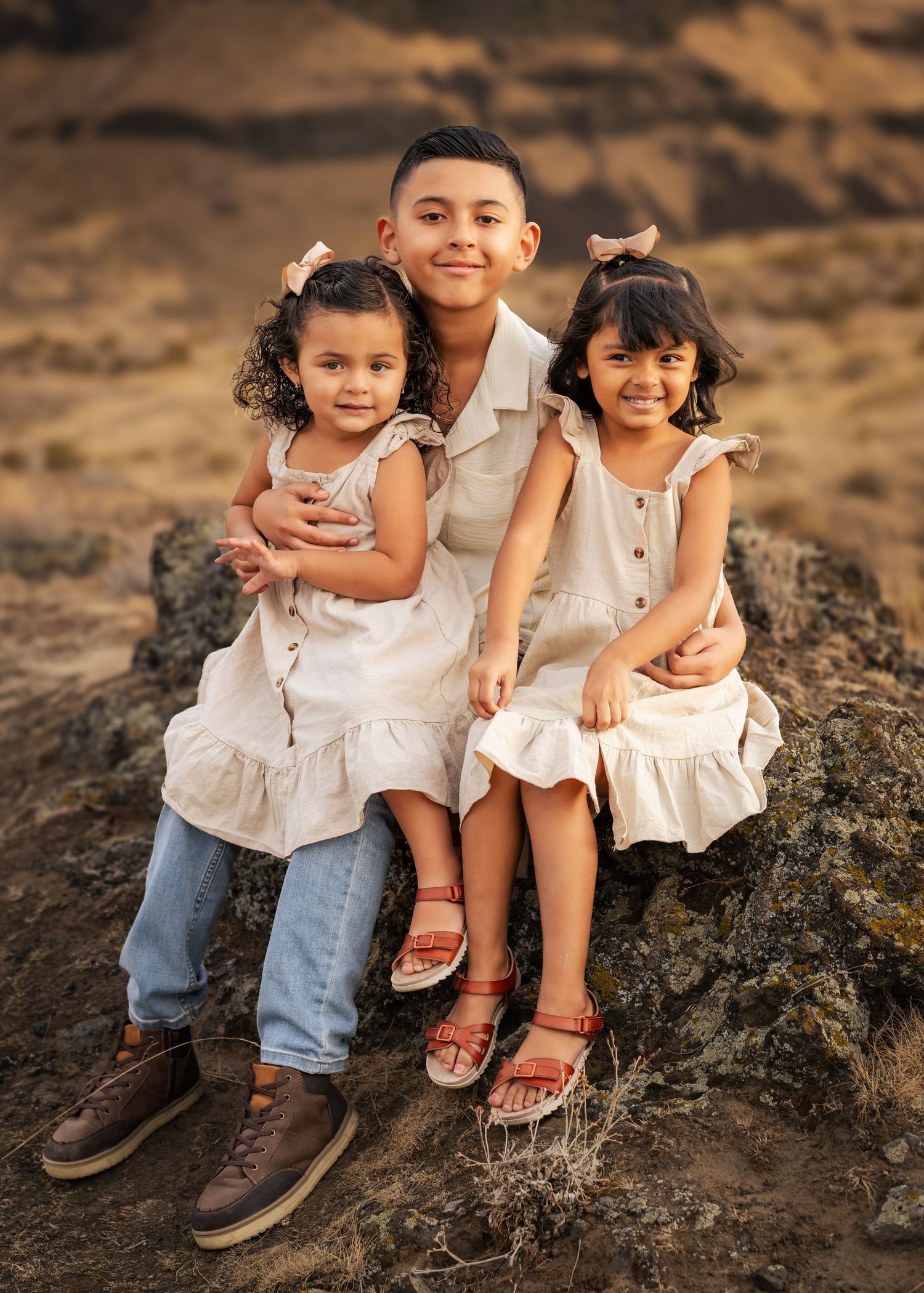 Three siblings in coordinated white outfits pose on desert rocks at sunset. Kennewick, WA. Photographer.
