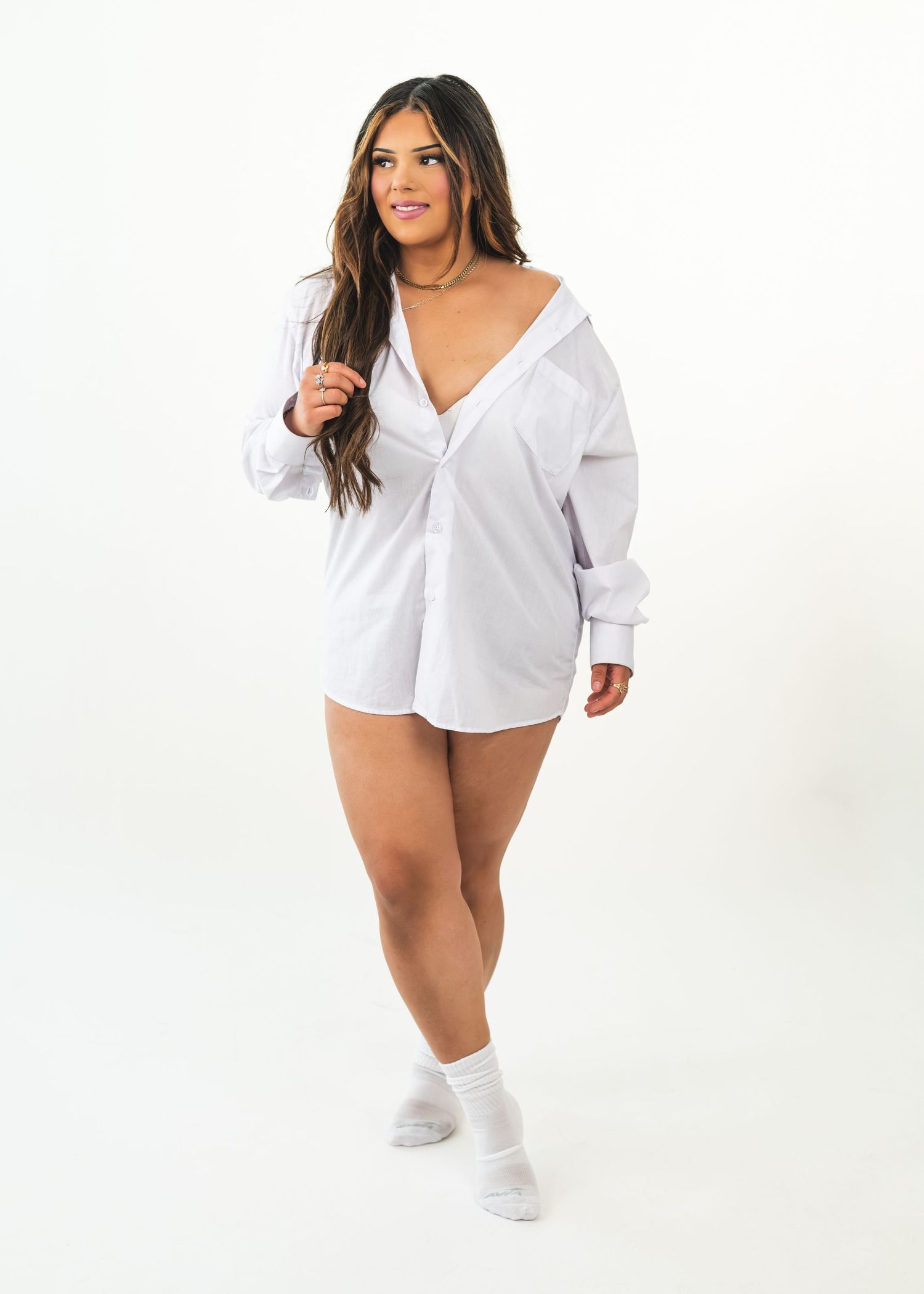 Woman wearing a white oversized button-down shirt dress with white socks, posing against a white background.
