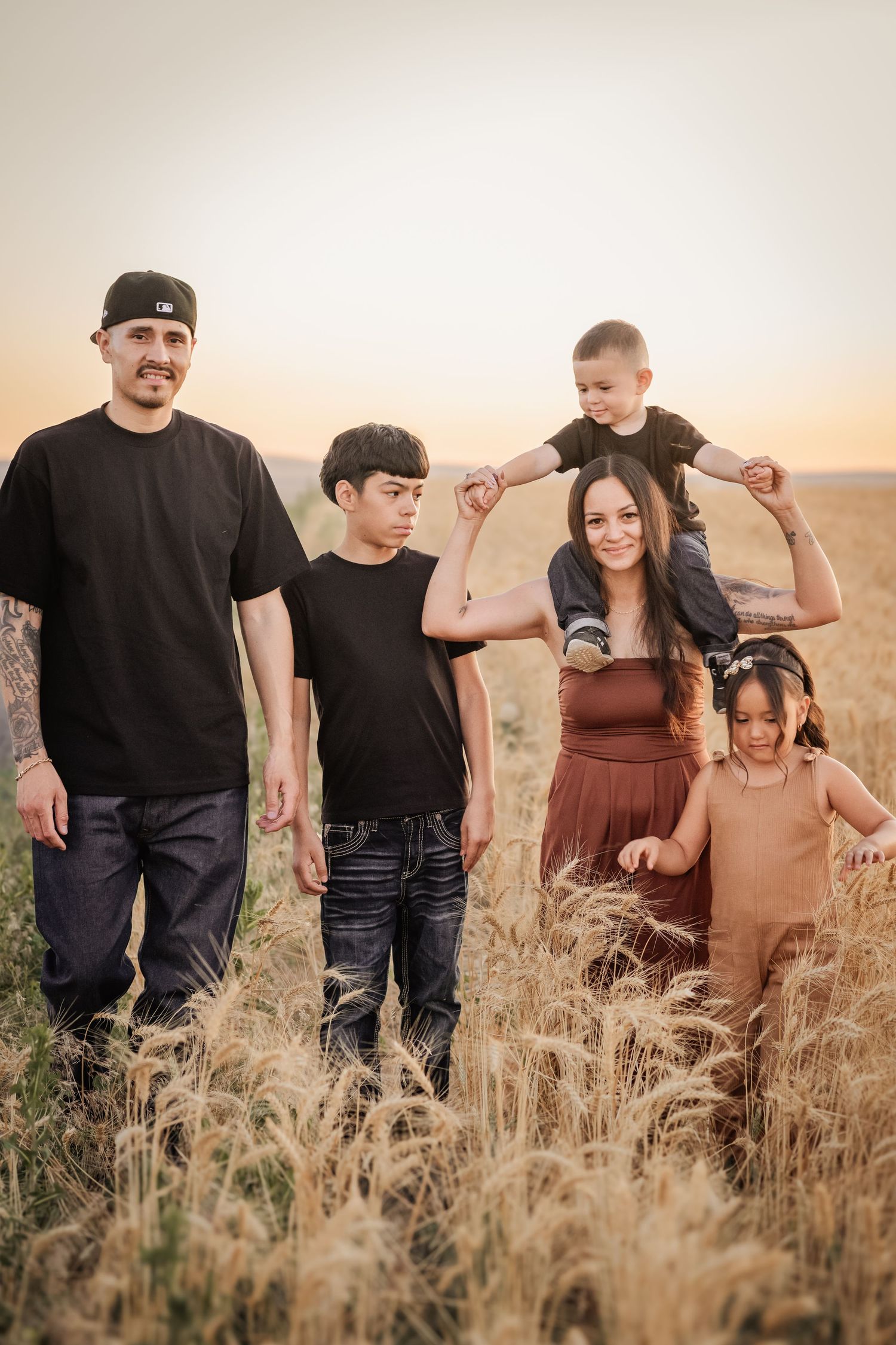 Family of five posing in golden wheat field at sunset, parents with three children enjoying outdoor portrait session.