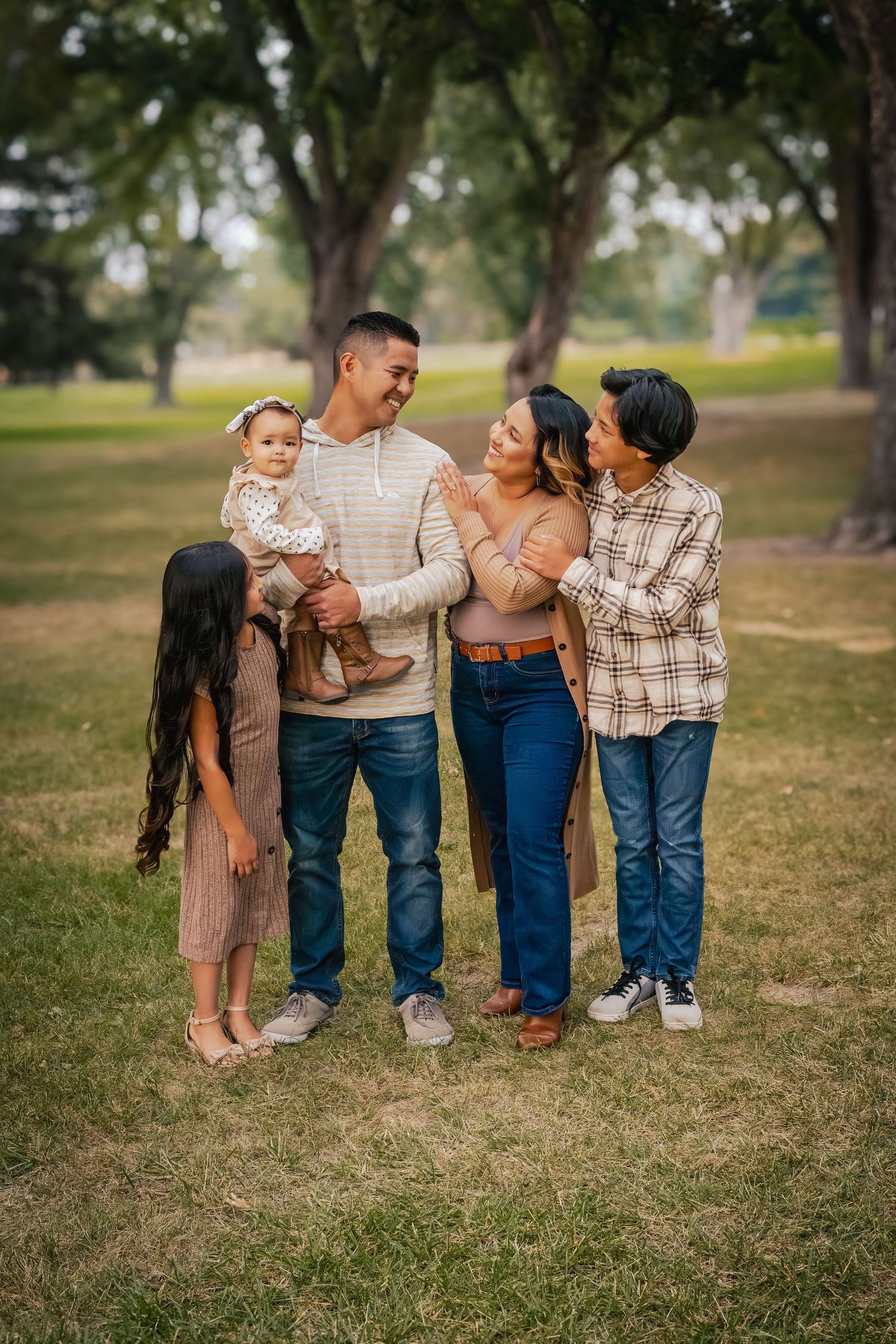 A family sits together on grass wearing coordinated casual outfits in warm earth tones during an outdoor photo session.