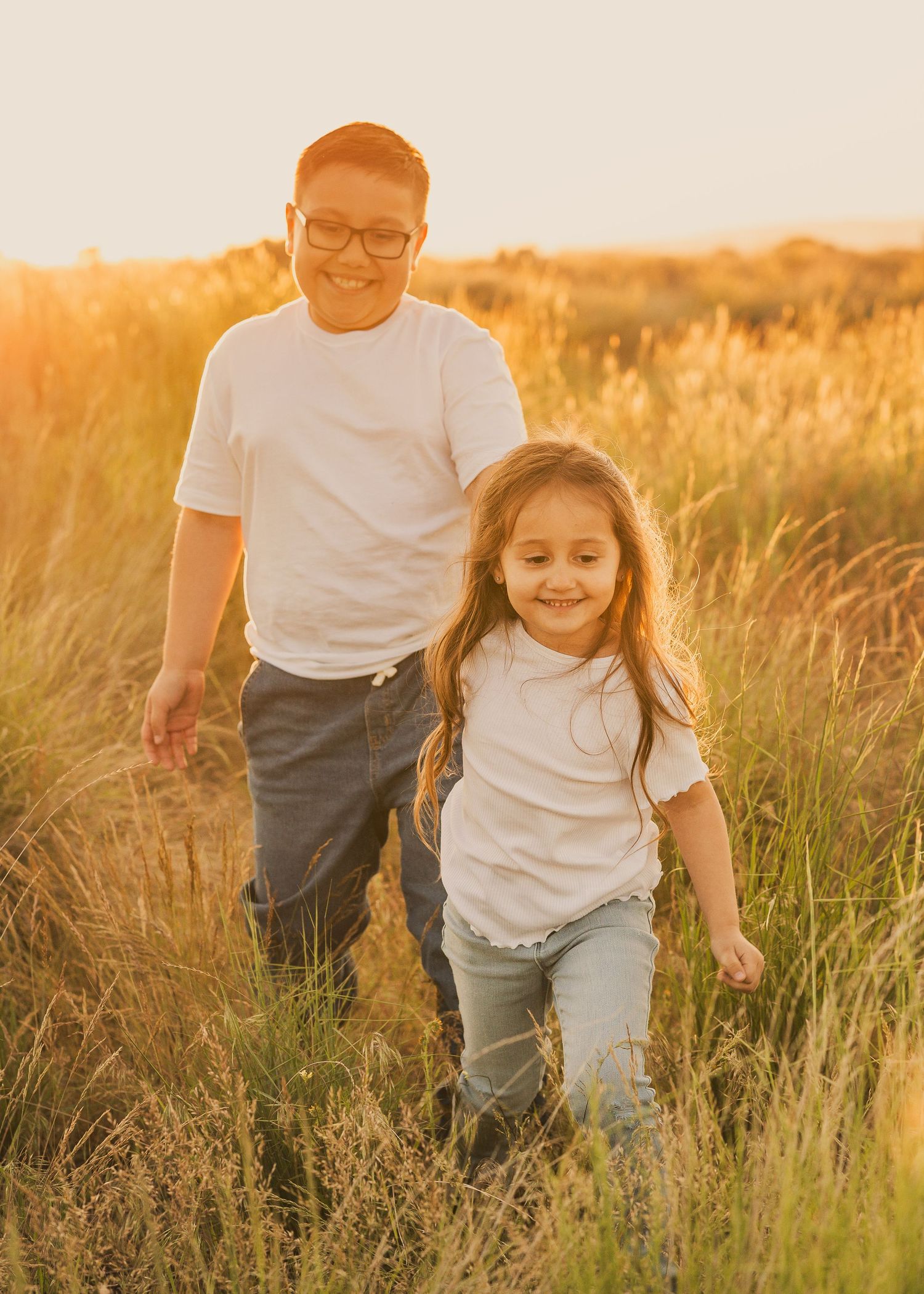 A parent and child run playfully through a golden field at sunset, creating a heartwarming silhouette against the warm sky.
