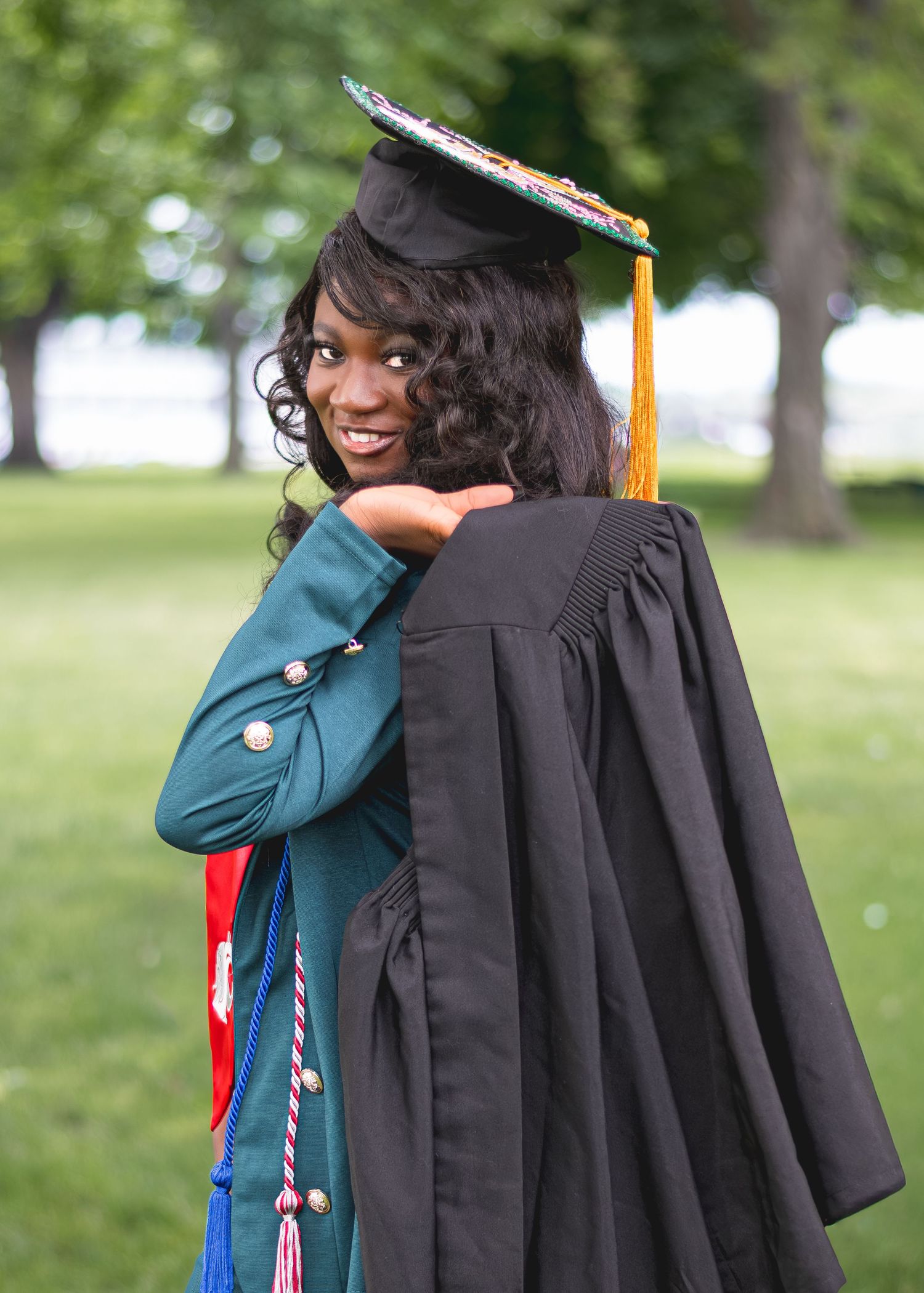 A smiling graduate in cap and gown hugs another person outdoors during a graduation ceremony.