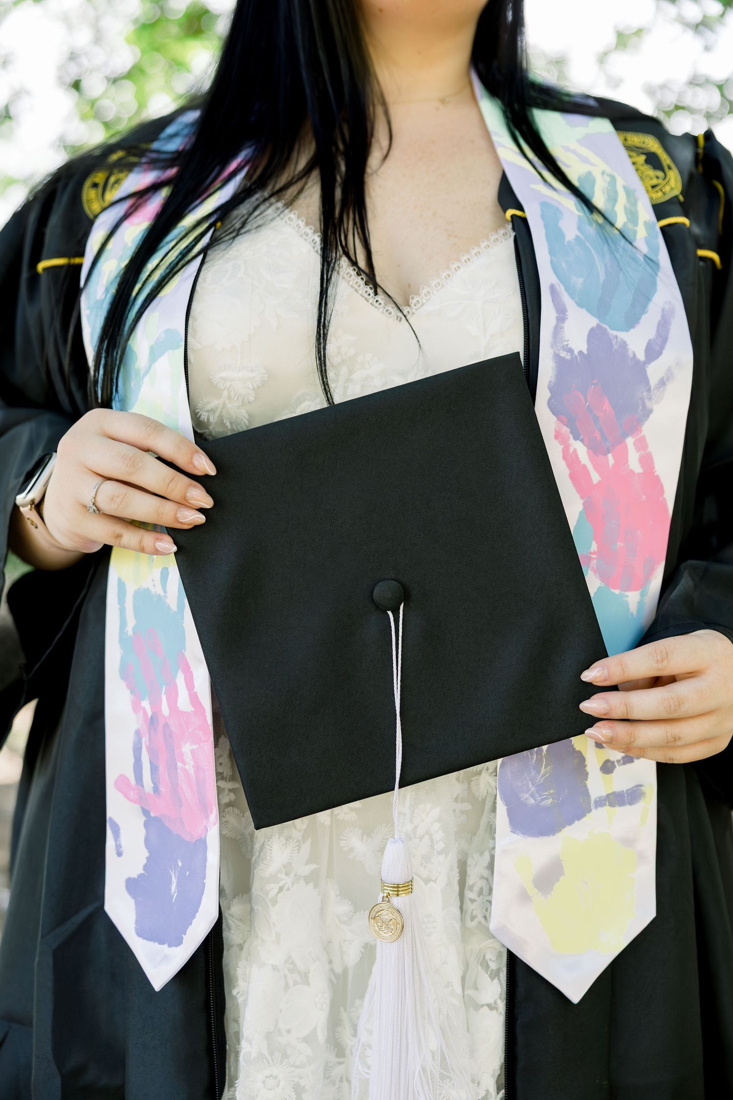 Graduation photo showing black gown with colorful handprint sash and diploma.