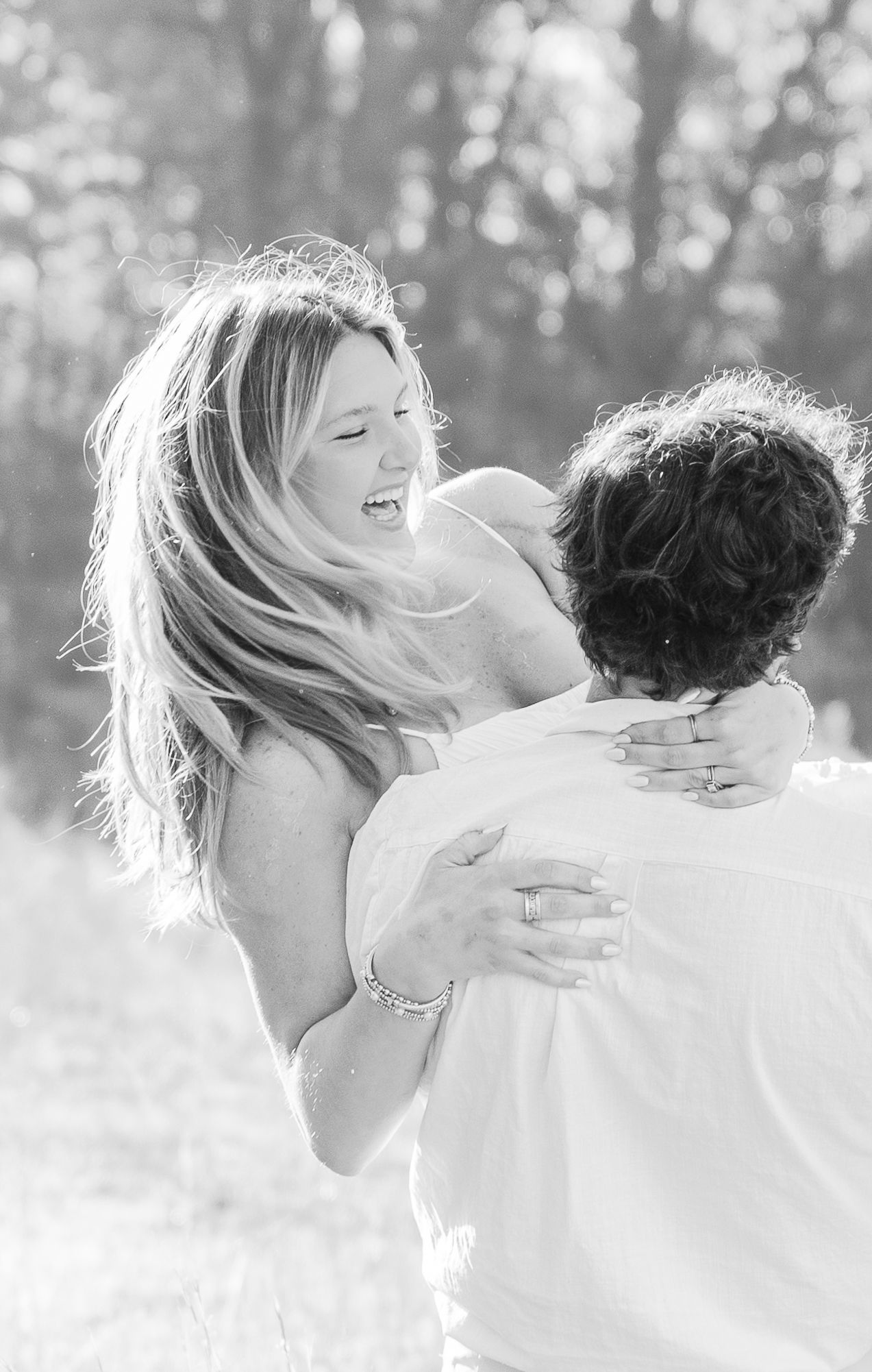 Black and white capture of joyful couple embracing and laughing in natural setting.