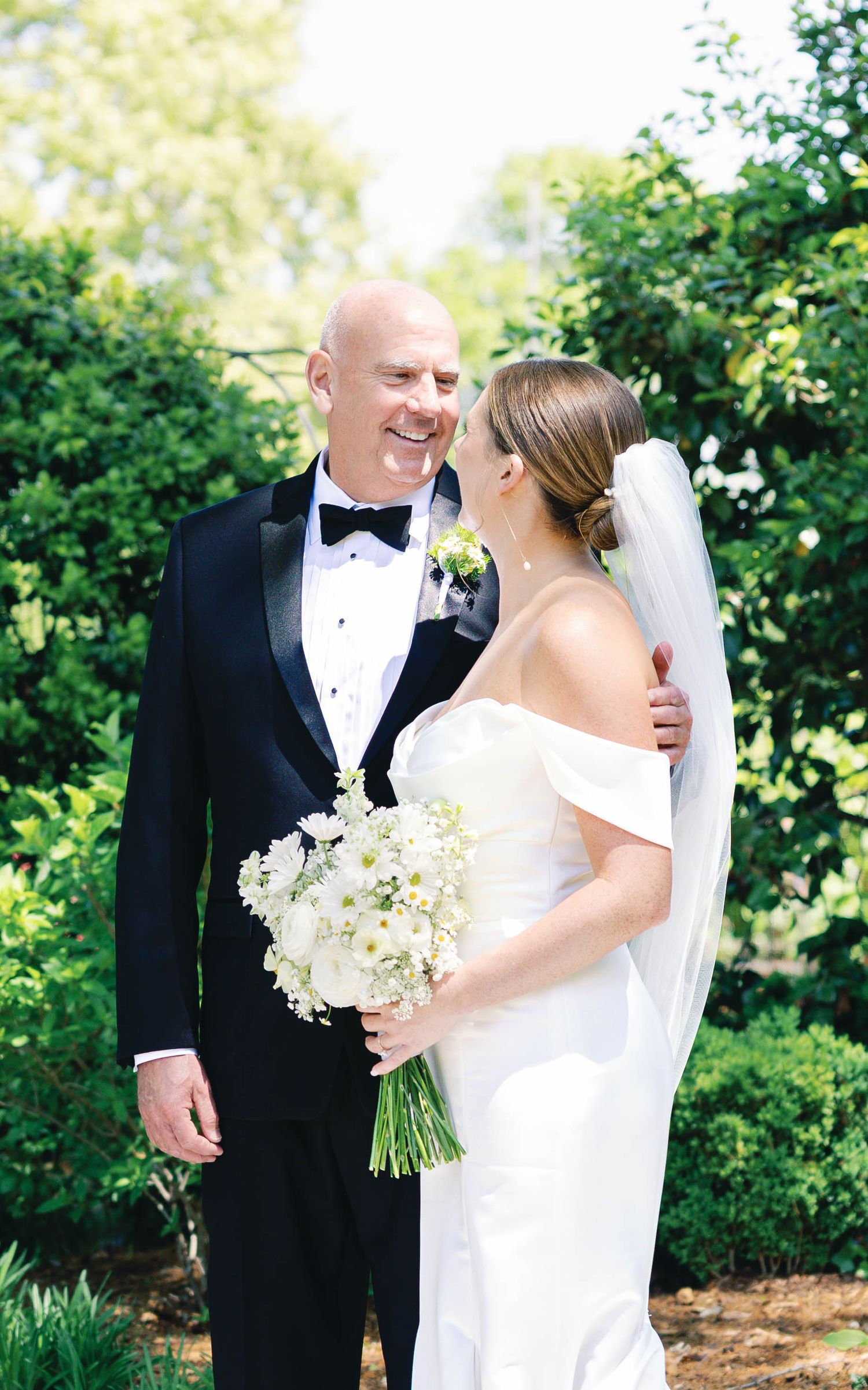 Elegant wedding couple shares intimate moment outdoors with white bouquet of flowers.