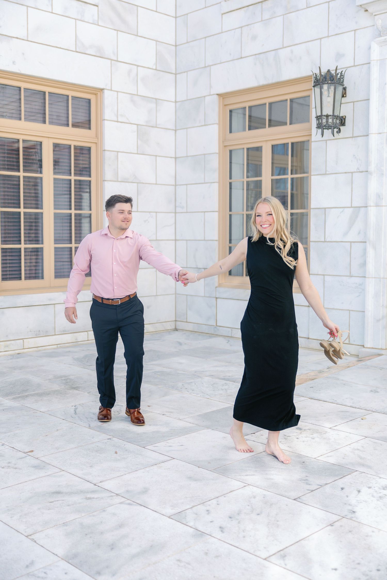 Playful couple holding hands while dancing on elegant white stone patio.