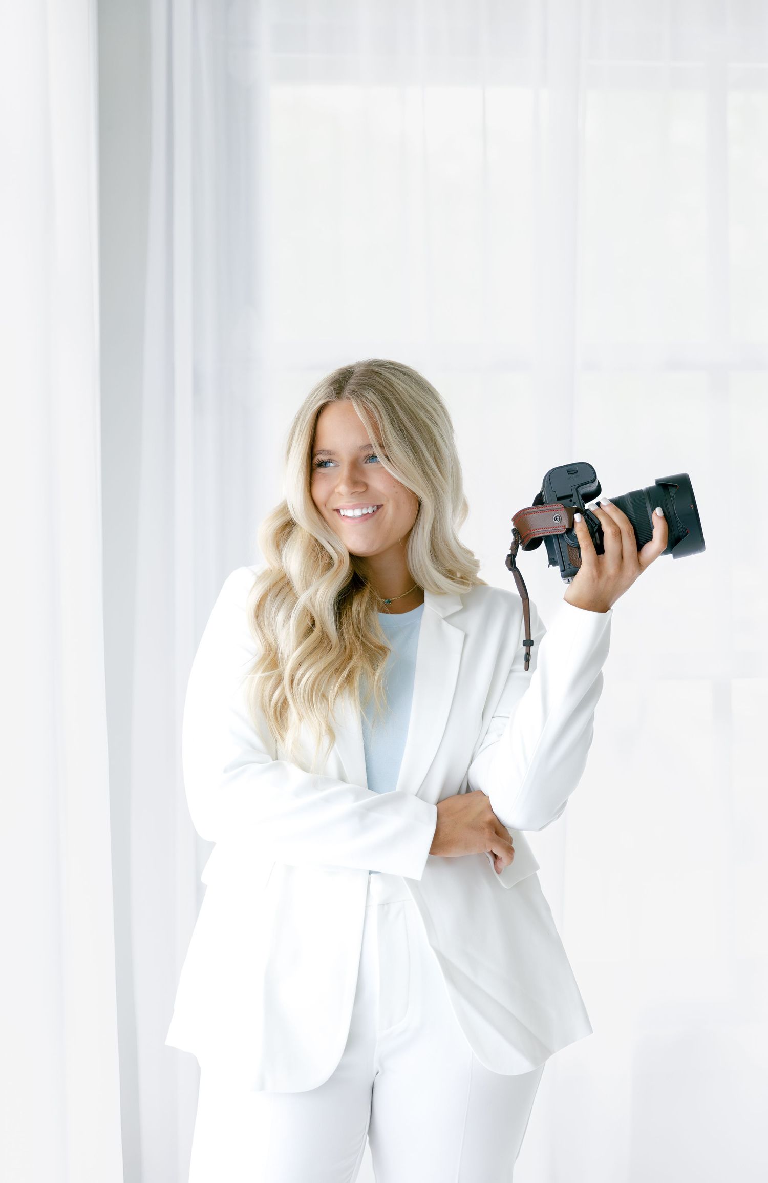 Professional photographer in crisp white suit holding DSLR camera against bright minimalist background.