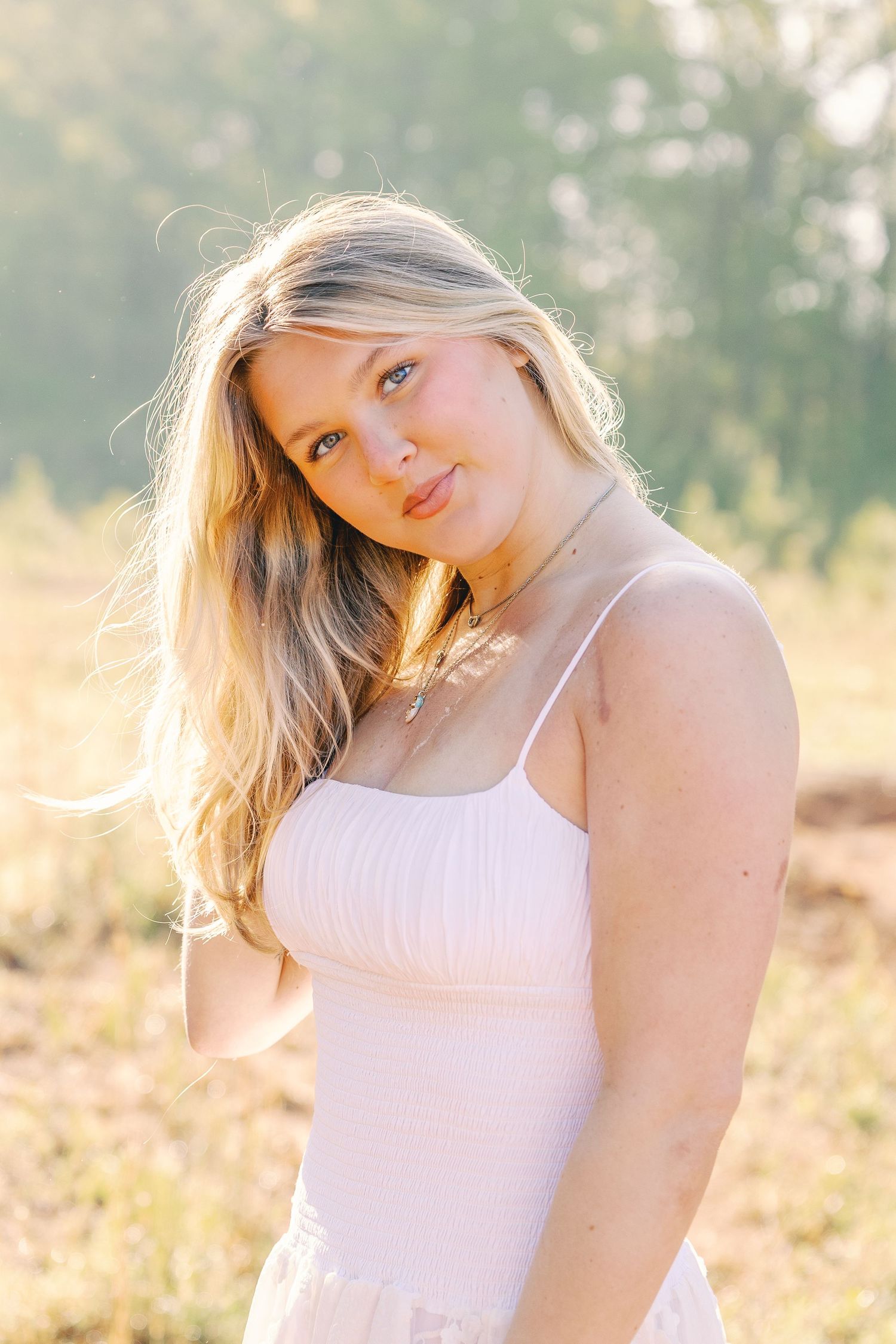 Woman in white dress poses against warm sunlit background with natural lighting.