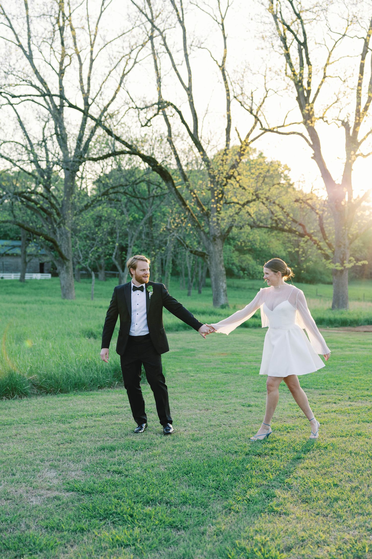 A playful dance moment between two people in formal attire on a green lawn.