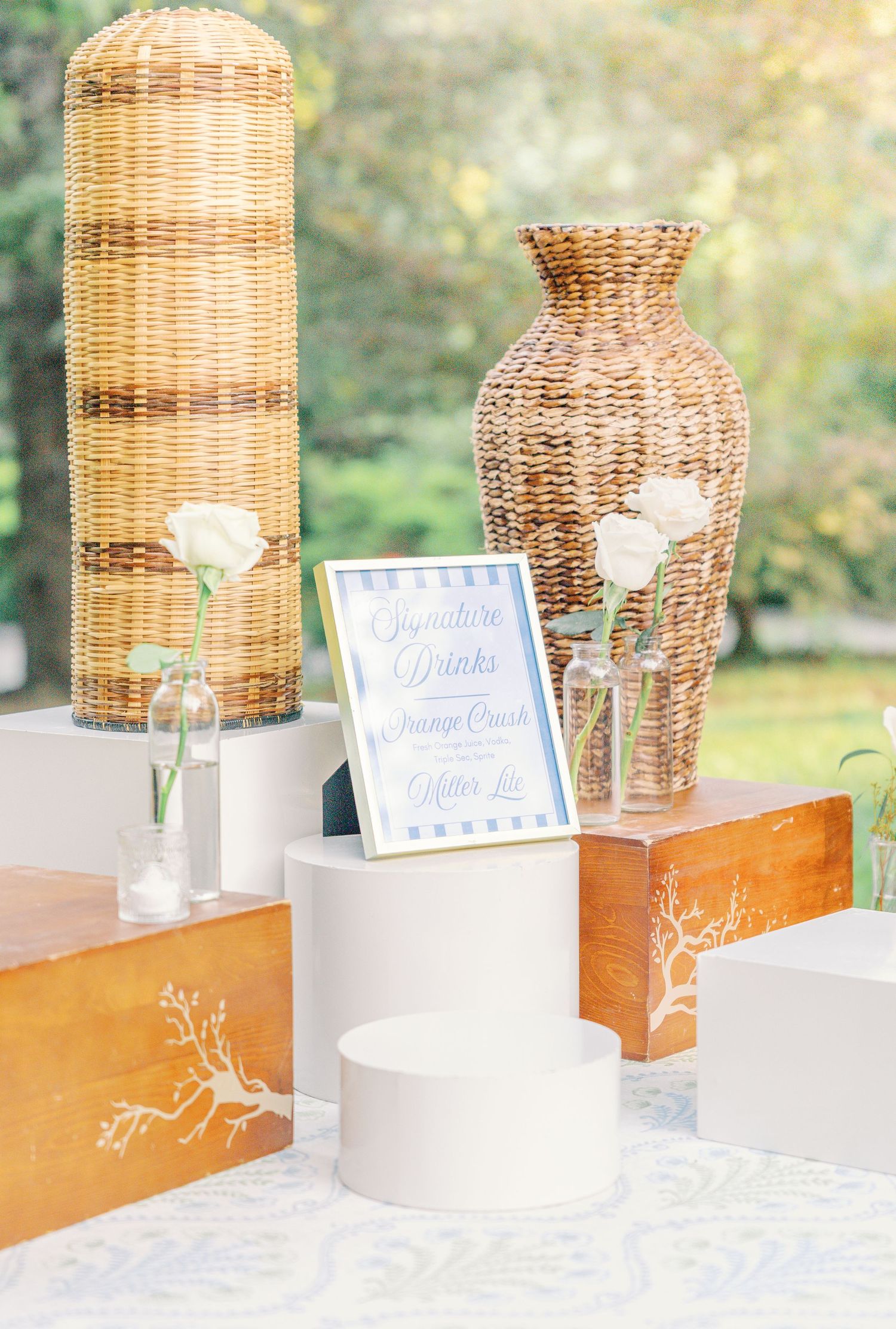 Wicker lamp shades decorate a long white and wooden table display at an outdoor event setting.