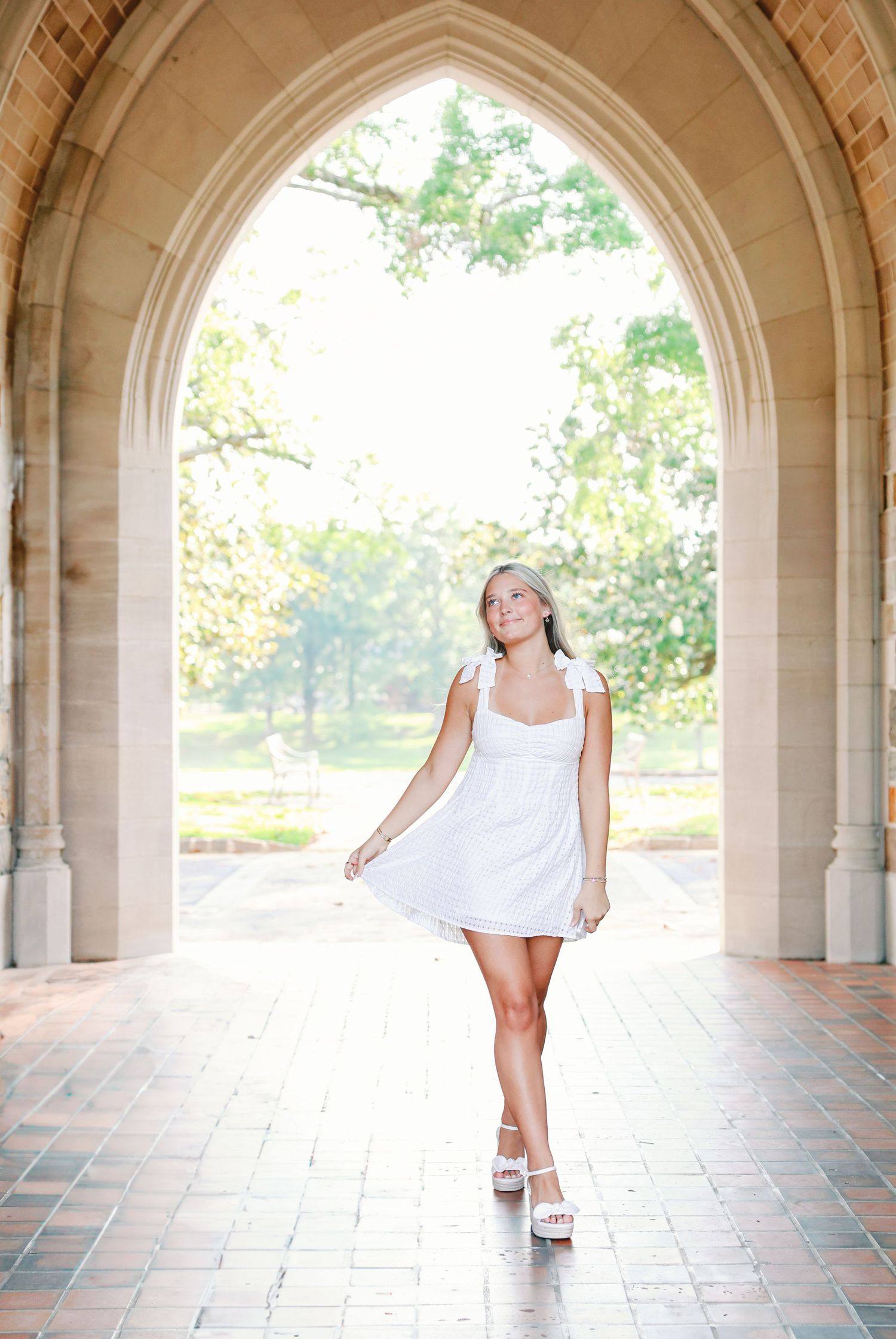 A graceful pose in a white summer dress beneath a Gothic stone archway creates an ethereal outdoor portrait.
