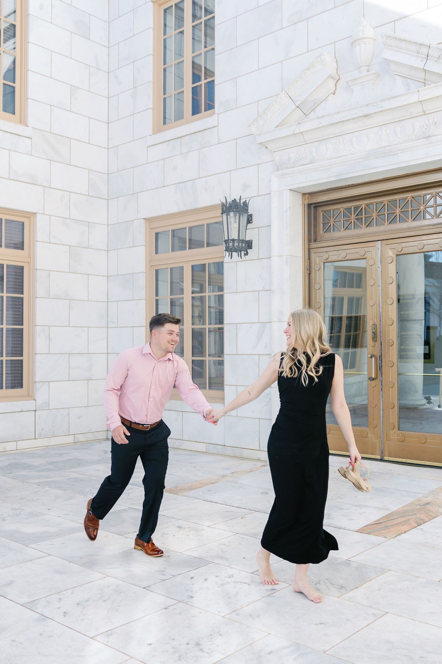 Couple dancing on white marble patio wearing pink shirt and black dress.