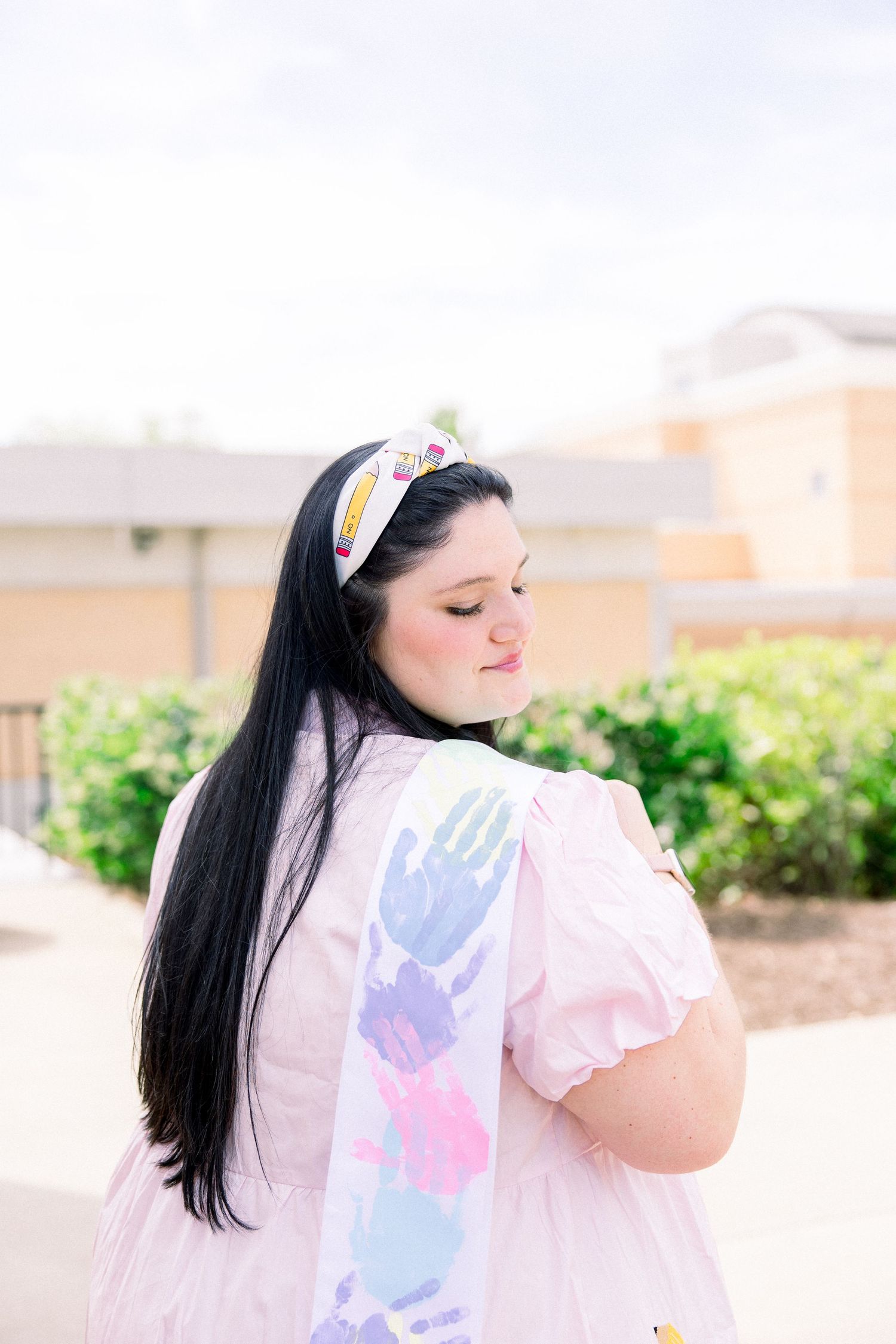Person in pink dress with handprint-decorated sash posing outdoors.